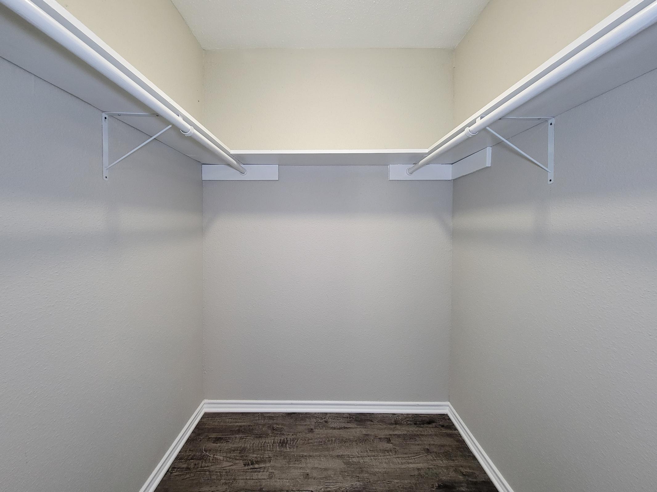 An empty closet with light-colored walls, wooden floor, and two white shelves mounted on the walls. The space is unoccupied, providing a clean and minimalistic appearance.
