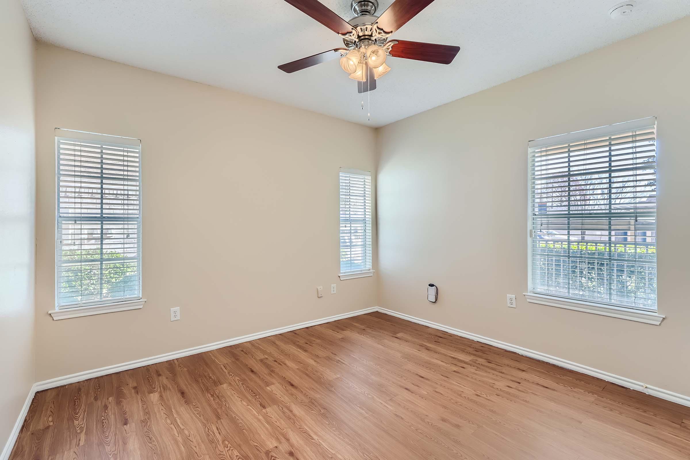 A living room at Rise Skyline with wood-style flooring, a ceiling fan, and windows. 
