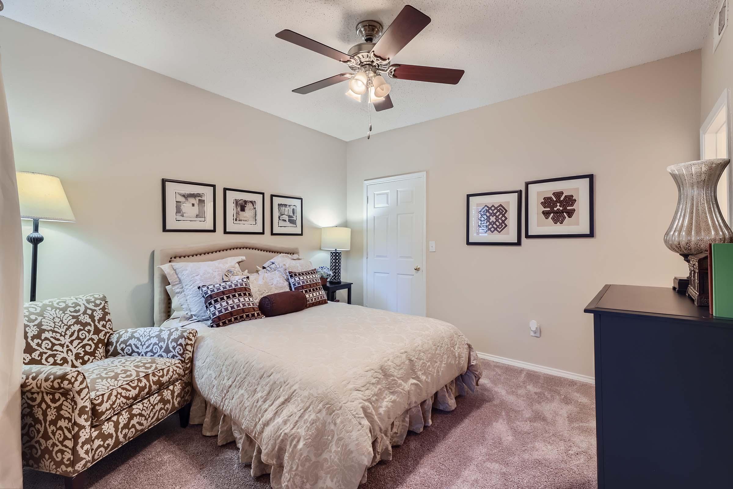A model carpeted bedroom with a queen bed and a ceiling fan at Rise Skyline.
