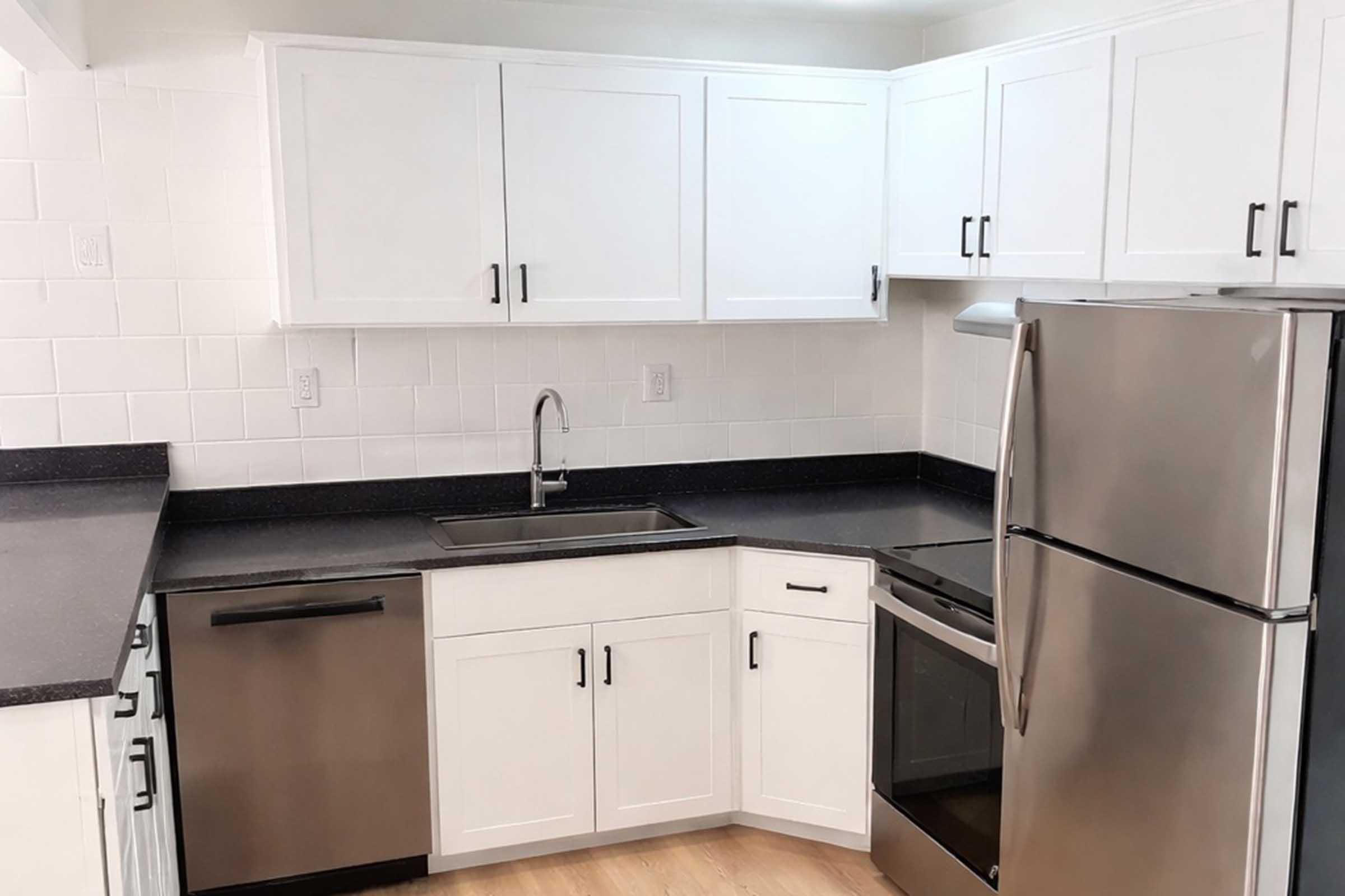 A modern kitchen featuring white cabinets, a stainless steel refrigerator, a dishwasher, and an oven. The countertops are black with a sleek finish, and the walls are adorned with white tiles. The space is bright and clean, designed for functionality and style.