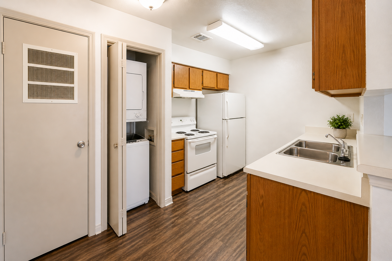 View of a modern kitchen featuring wooden cabinets, a white stove and refrigerator, a sink, and a laundry area behind a door. The flooring is a dark wood finish, and there's a small plant on the counter, adding a touch of decor to the space. The lighting is bright and welcoming.