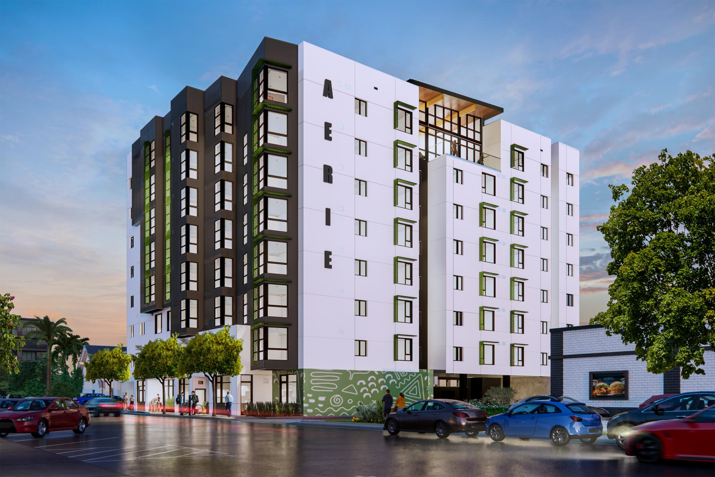 Modern multi-story building named "Aerie," featuring a sleek design with white and dark green accents. Trees and landscaping are visible in the foreground, along with parked cars. The sky is a soft blue with hints of sunset, creating a vibrant backdrop for the structure.