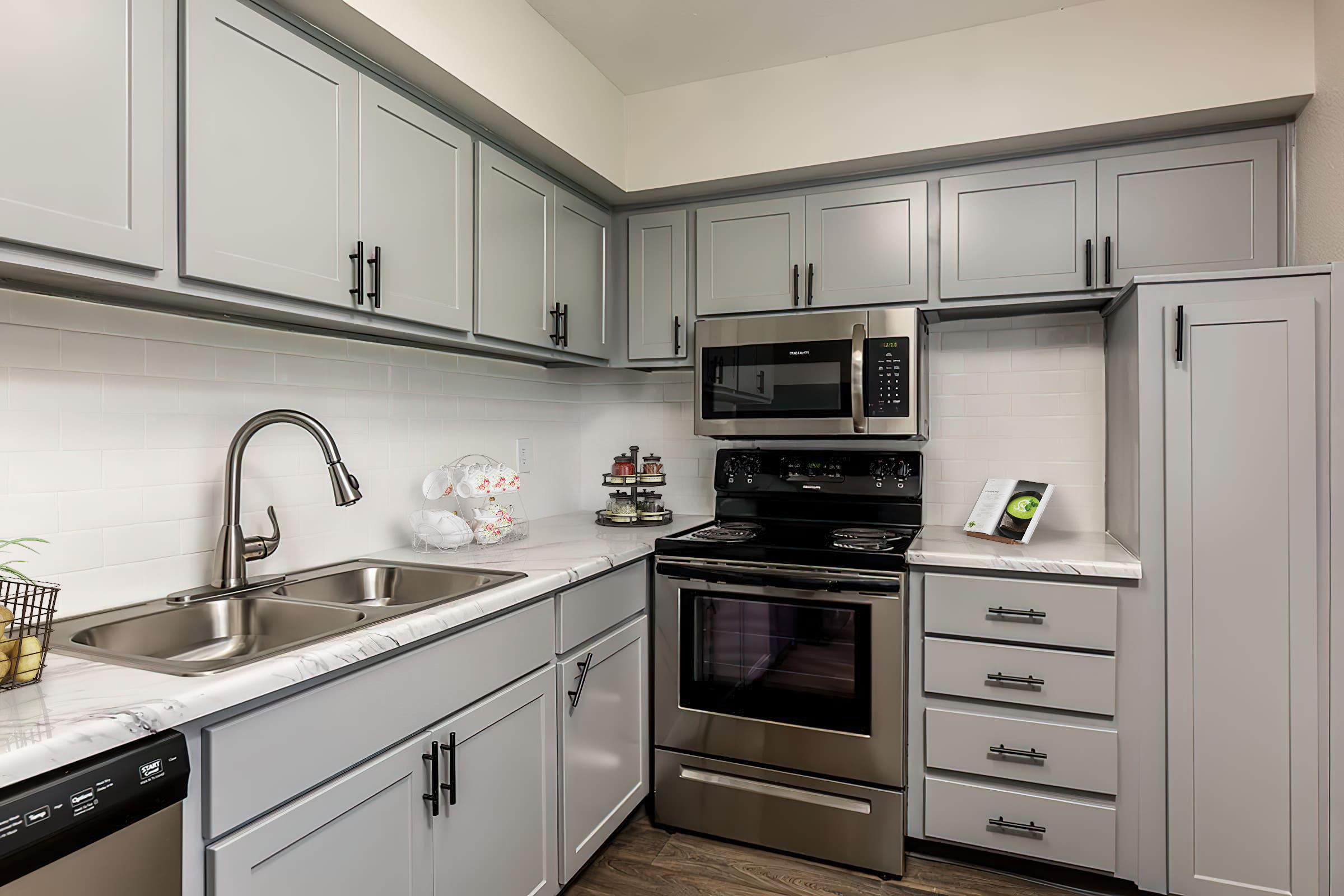 Modern kitchen featuring gray cabinets, stainless steel appliances, a double sink, and a marble countertop. The space includes a built-in microwave, an oven, and a sleek design with decorative items on the counter, creating a clean and contemporary look.