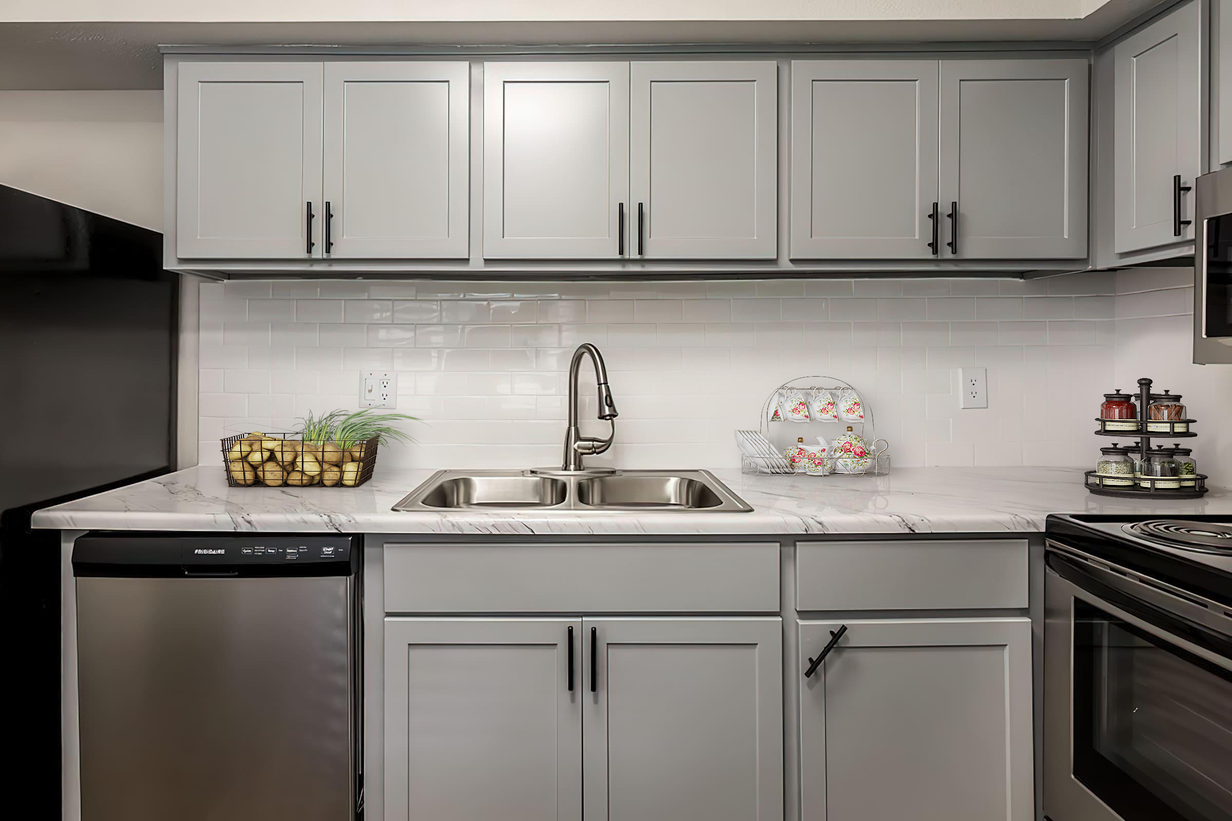 Modern kitchen featuring gray cabinets, a double sink with a stylish faucet, and a marble countertop. To the left, there is a stainless steel dishwasher. A small decorative bowl with fruit and a tiered stand with neatly arranged cupcakes are displayed on the counter, adding a touch of color and charm.
