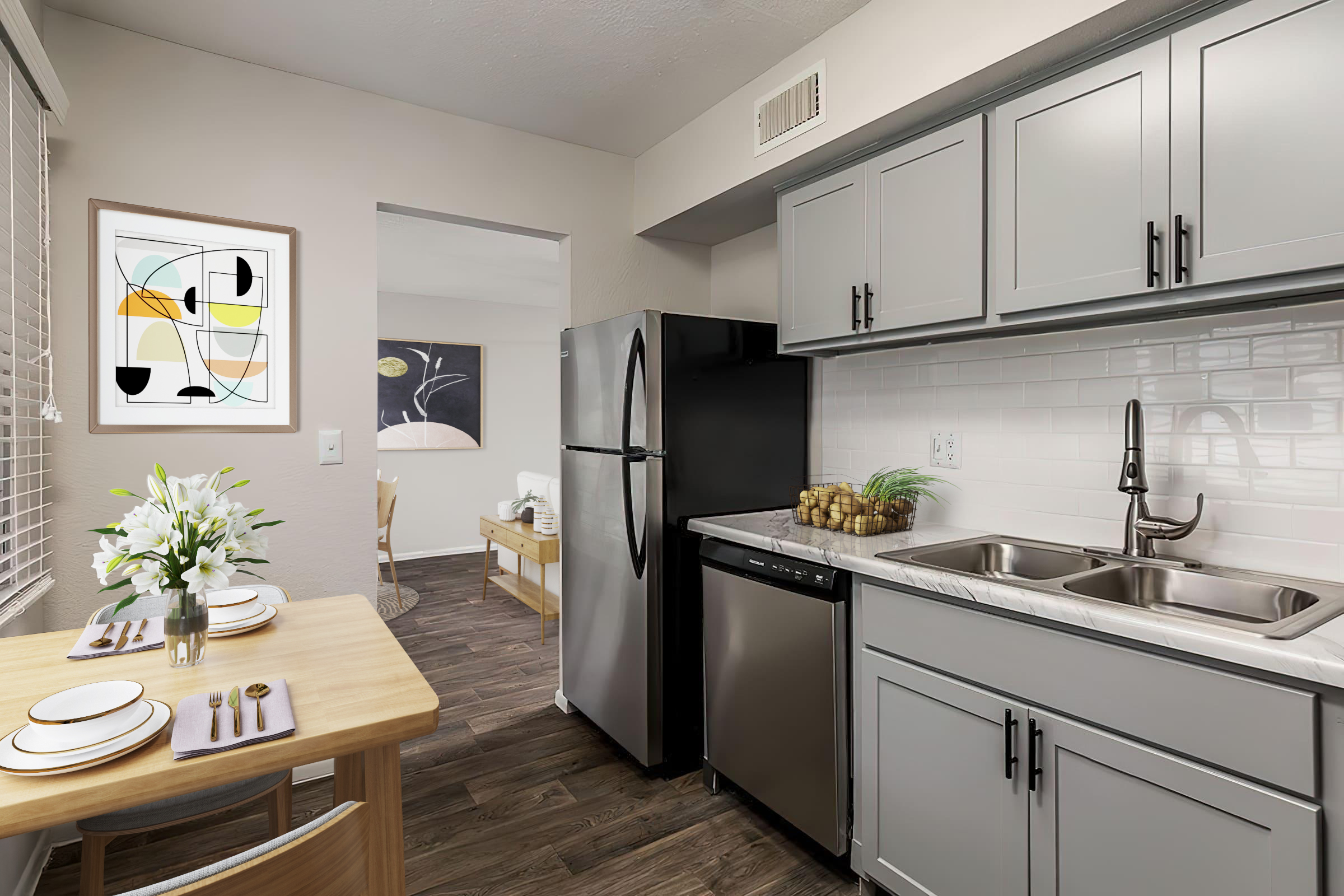 Modern kitchen featuring gray cabinets, stainless steel appliances, and a double sink. A wooden dining table is set with dishes and utensils. Bright artwork hangs on the wall, and natural light streams in through a window. The overall decor is contemporary and inviting.