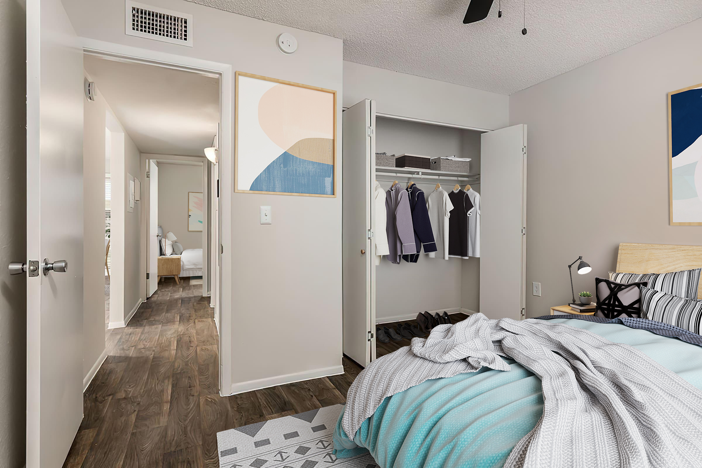 A well-decorated bedroom featuring a bed with a light blue and gray blanket. A closet is ajar, revealing neatly hung clothes. The room has modern artwork on the walls and a view into a hallway leading to another room, showcasing a cozy aesthetic with wooden flooring and soft lighting.