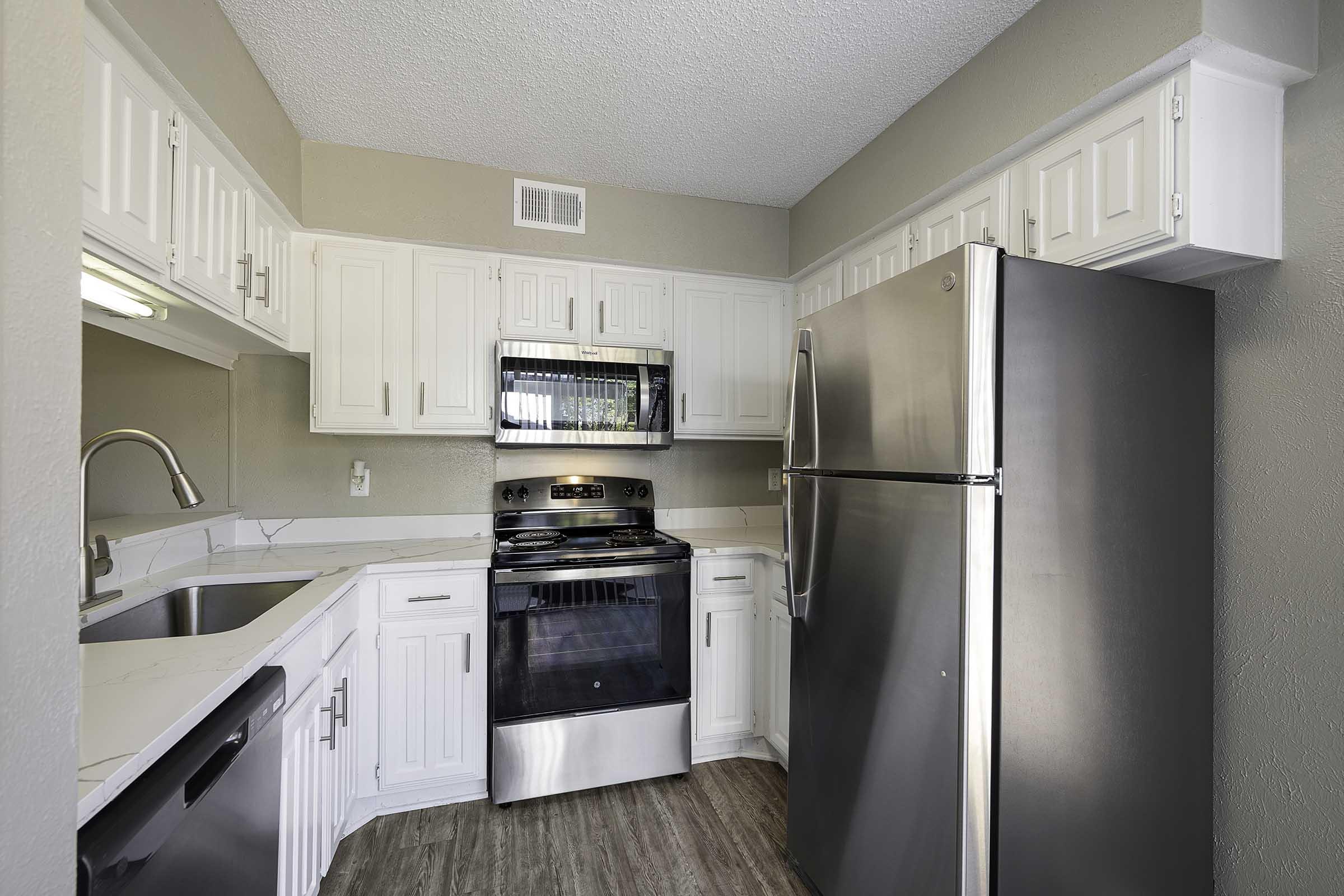 A modern kitchen featuring white cabinetry, a stainless steel refrigerator, and a black oven and stove. The space includes a double sink and light-colored countertops, with a neutral wall color and wood-look flooring, creating a bright and inviting atmosphere.