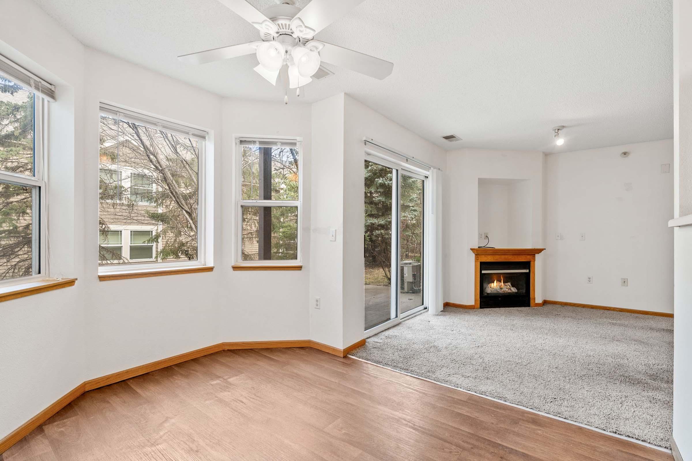Bright and airy living space featuring large windows that allow natural light, a ceiling fan, and a cozy fireplace. The flooring is a mix of carpet and wood, providing a warm atmosphere. A sliding glass door leads to an outdoor area, enhancing the connection to nature.