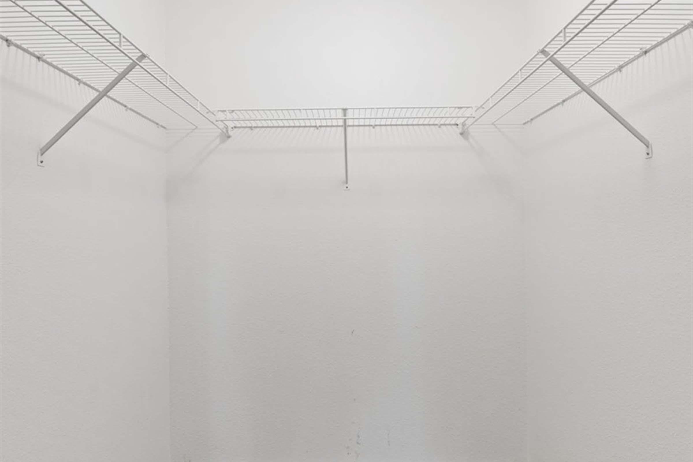 Empty white closet with wire shelving mounted on two walls, creating an open and spacious feel. The walls and floor are also white, contributing to a clean and minimalist appearance.