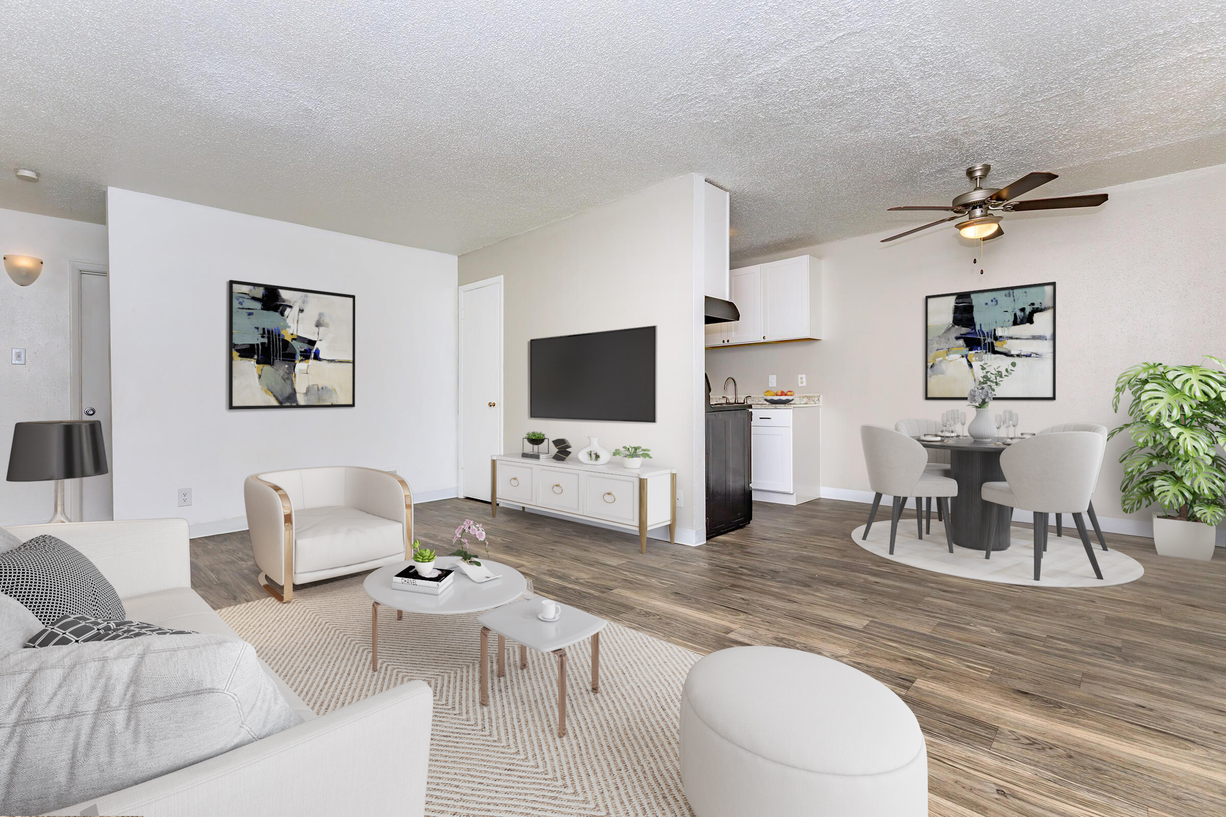 Modern living room and dining area featuring a cozy white sofa, a round coffee table, and a stylish side table. A large TV is mounted on the wall, with a dining set for four nearby. Decorative plants and abstract artwork adorn the walls, creating a welcoming and contemporary atmosphere.