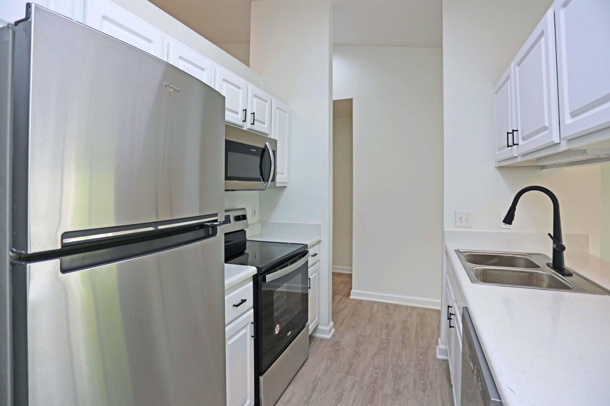 A modern kitchen featuring stainless steel appliances, including a refrigerator, oven, and microwave, set against white cabinetry. The countertops are light-colored, and the flooring is a wood-like laminate, creating a bright and inviting space with ample cabinet storage.