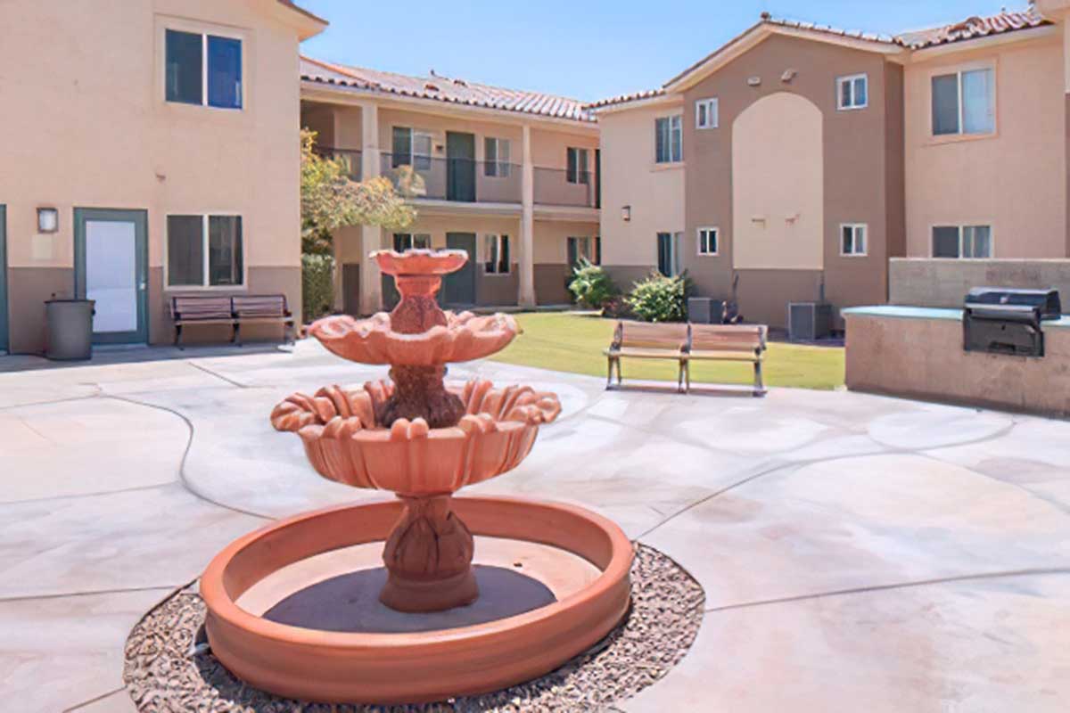 A courtyard area featuring a central terracotta fountain surrounded by a landscaped lawn.