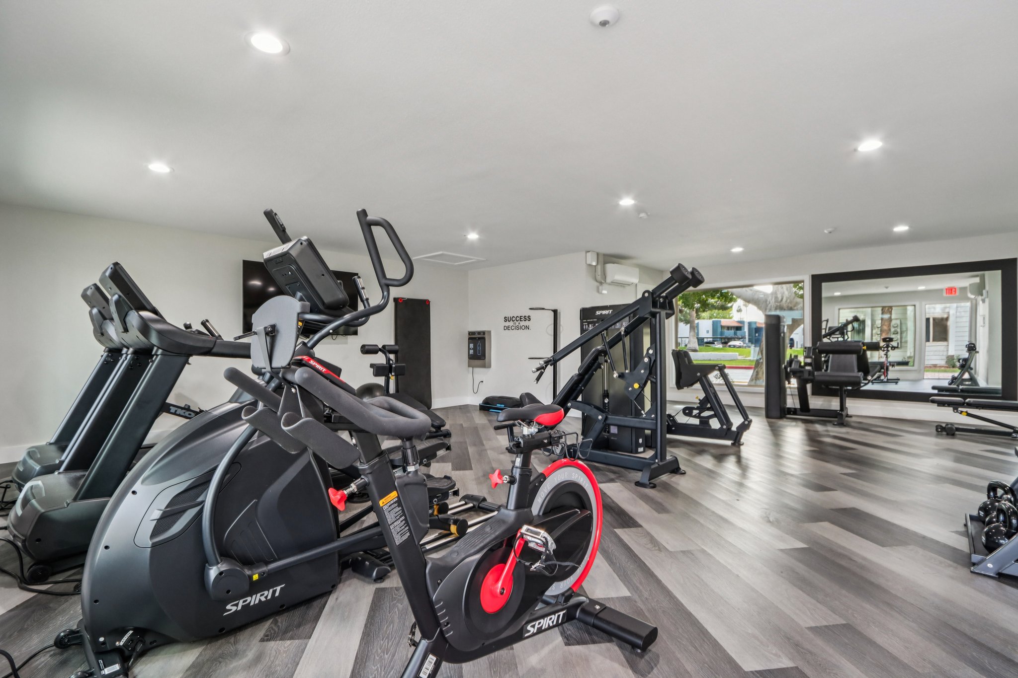 A modern gym space featuring various exercise equipment, including stationary bikes, treadmills, and weight machines. The room is well-lit with sleek flooring and a clean, organized layout, suitable for workouts.