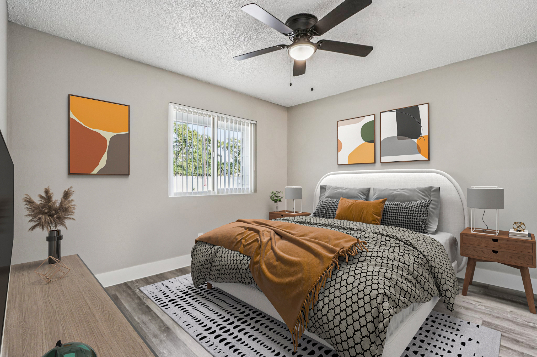 A cozy bedroom featuring a large bed dressed in patterned linens with an orange throw. There are two abstract artworks on the wall, a nightstand with a lamp on each side of the bed, and a stylish rug. A window allows natural light to brighten the space, complemented by a ceiling fan.