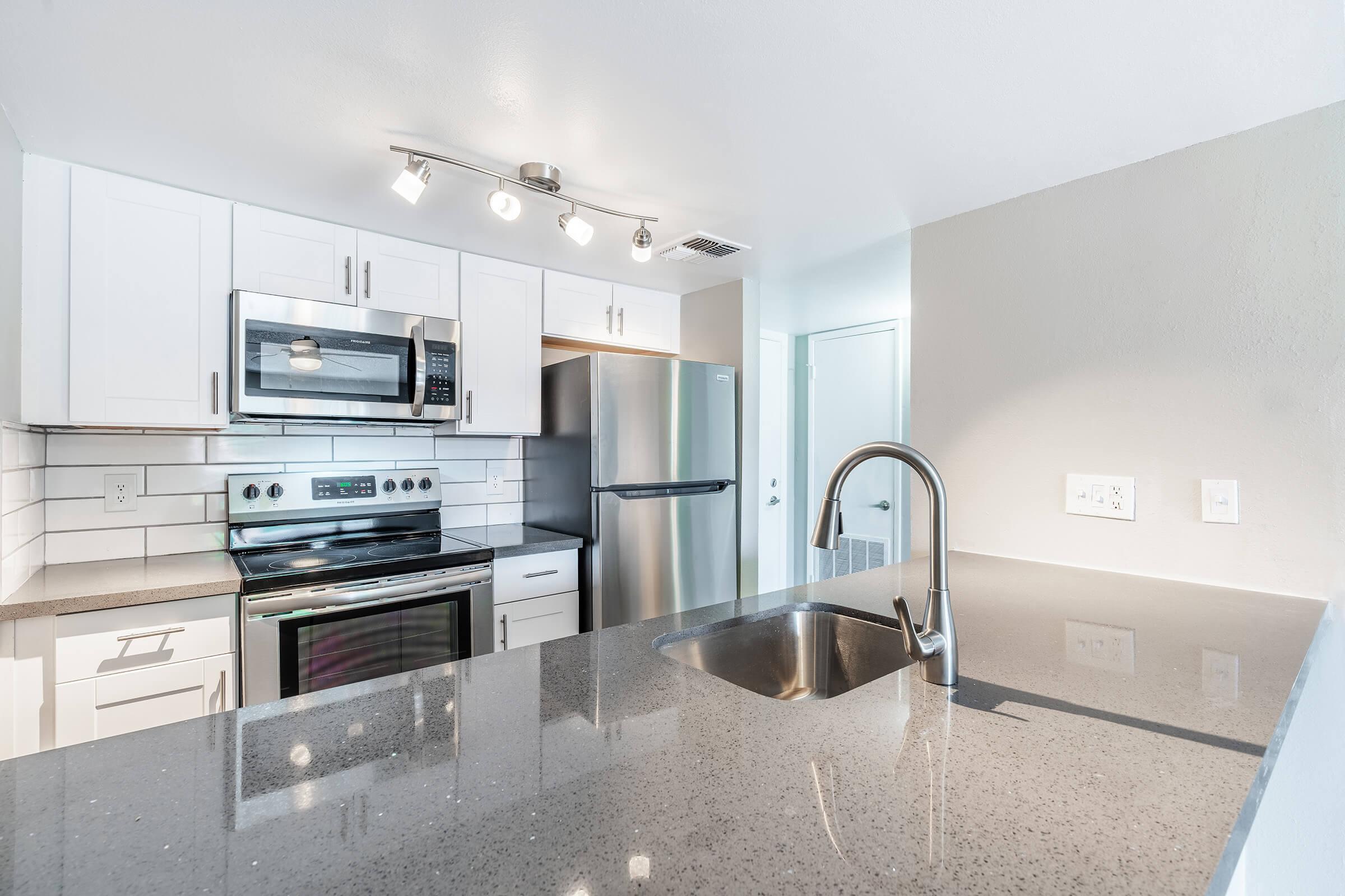 Modern renovated kitchen with large quartz island, white cabinets, and stainless steel appliances in a Mesa apartment for rent