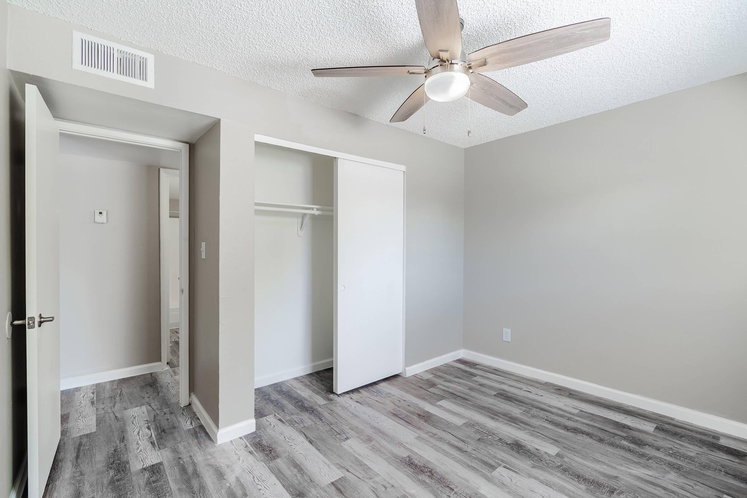 Spacious modern Mesa apartment bedroom with ceiling fan, closet, grey wood flooring, and doorway
