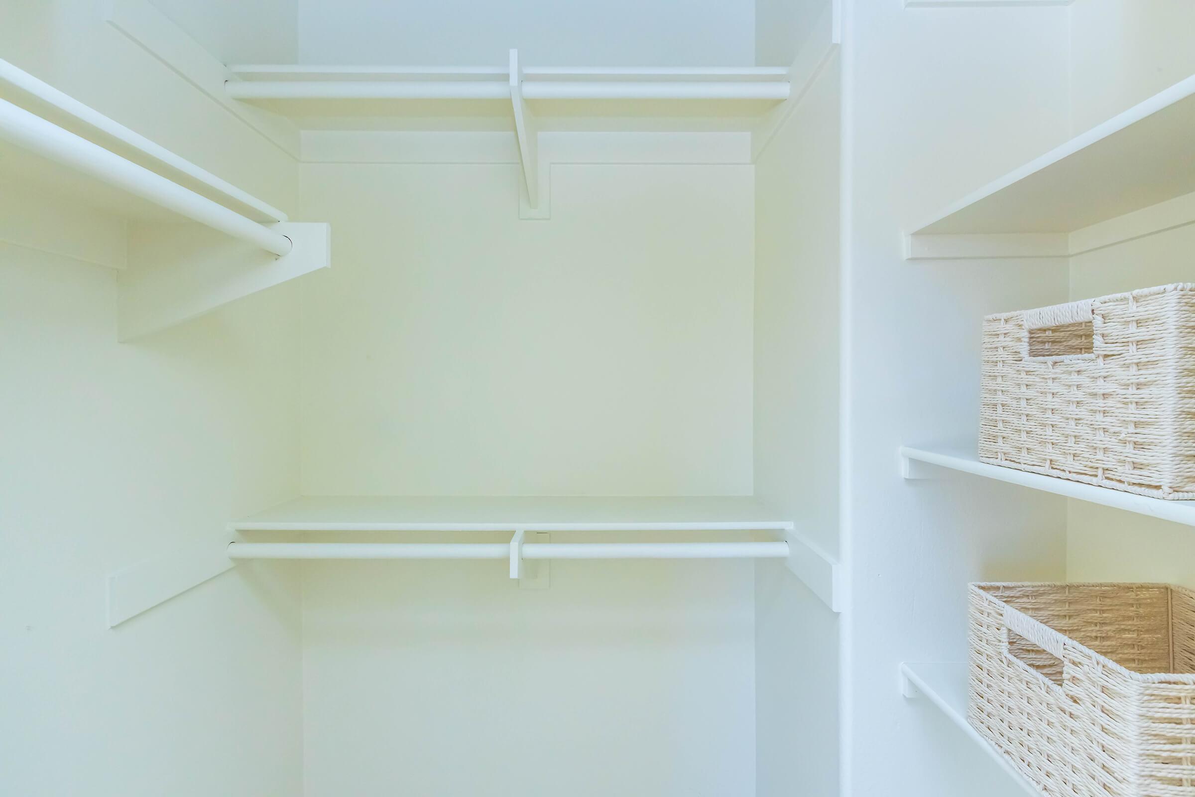 Empty closet space featuring white walls and shelves. There are two horizontal clothing rods on the left side and two woven baskets on the right, sitting on a shelf. The overall design is minimalistic and organized, with a bright and airy feel.