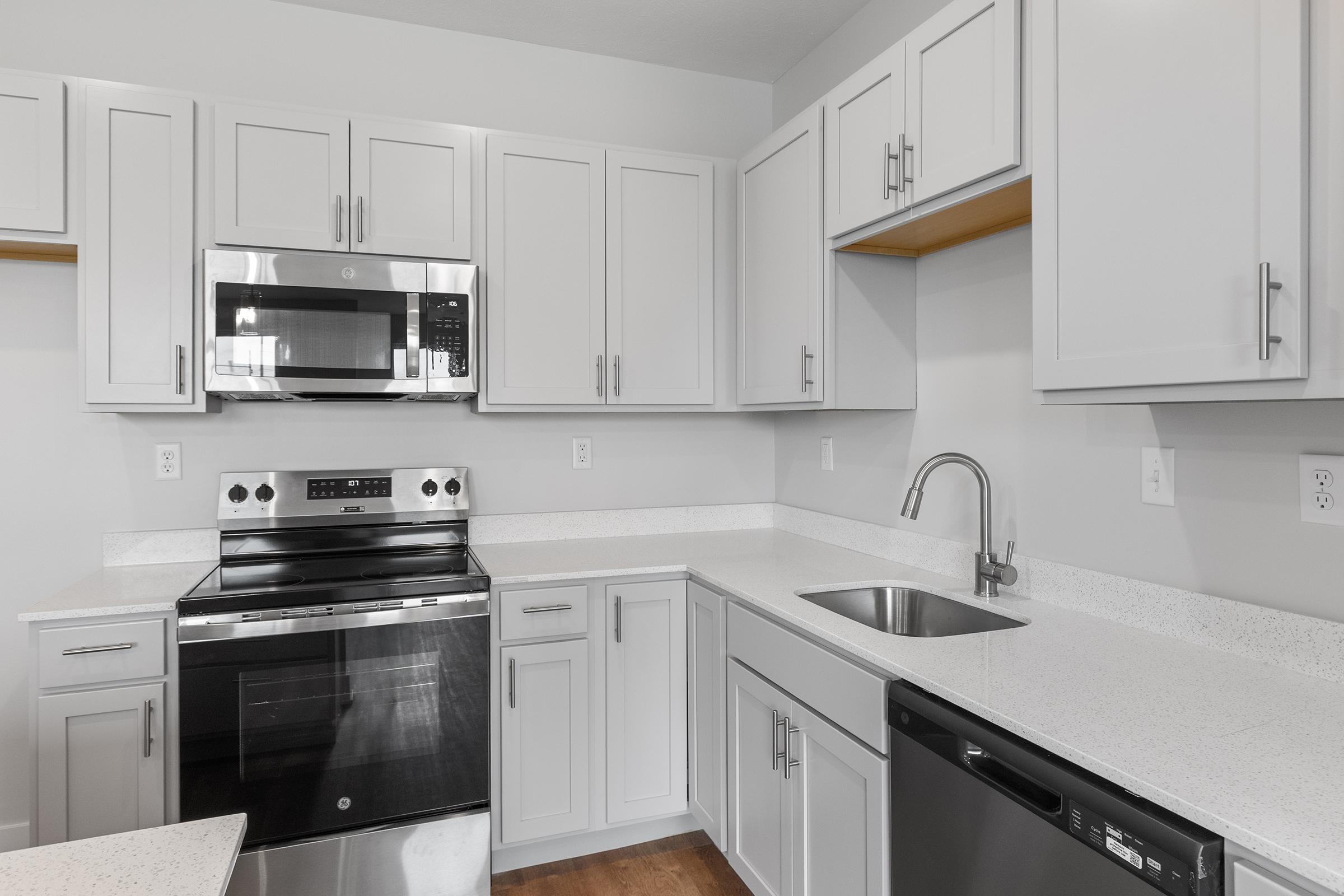 Modern kitchen featuring gray cabinets, stainless steel appliances including an oven, microwave, and dishwasher. A sink is situated between the dishwasher and a countertop with a light-colored surface, providing a clean and contemporary look.