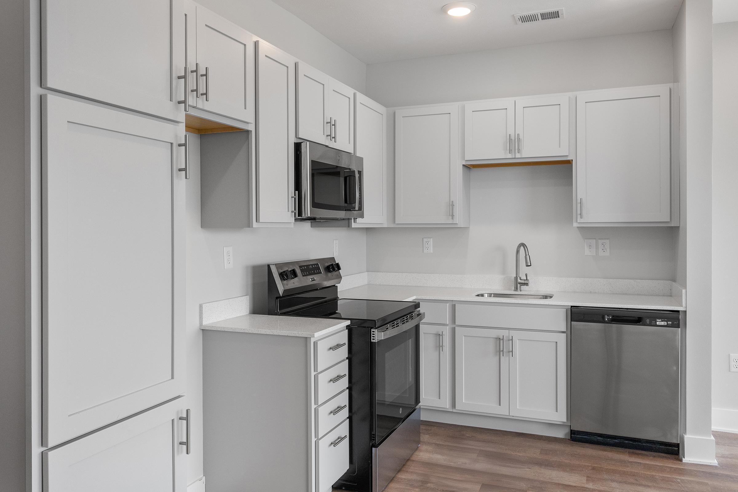 Modern kitchen featuring white cabinetry, stainless steel appliances including a microwave and dishwasher, a black stove, and a spacious countertop. The walls are light-colored, and the flooring is a warm wood tone, creating a bright and inviting atmosphere.