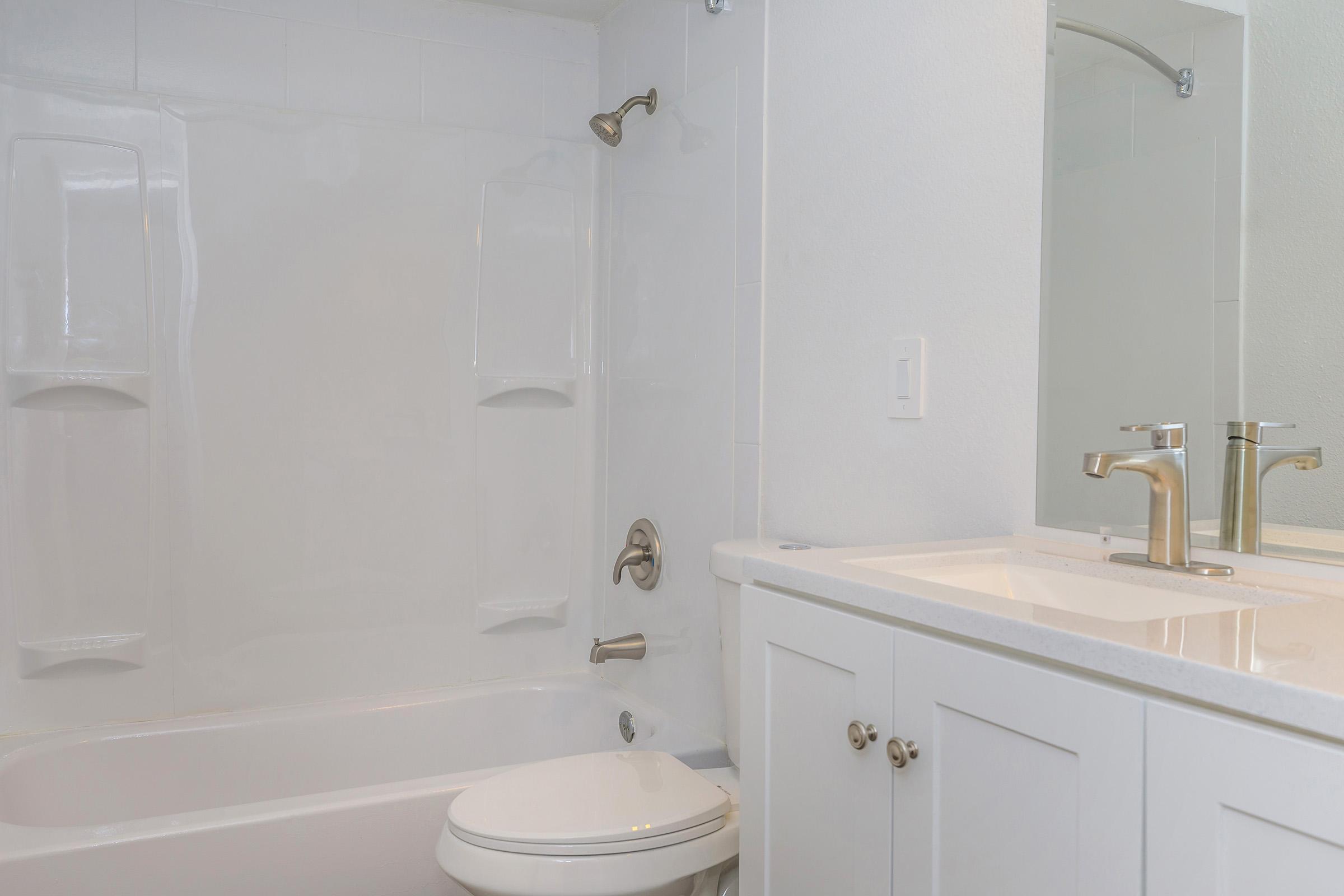 A clean, modern bathroom featuring a white bathtub and shower combination, a wall-mounted mirror, and a sink with elegant brass faucets. The walls are painted in a light color, and there are simple white cabinets under the sink.