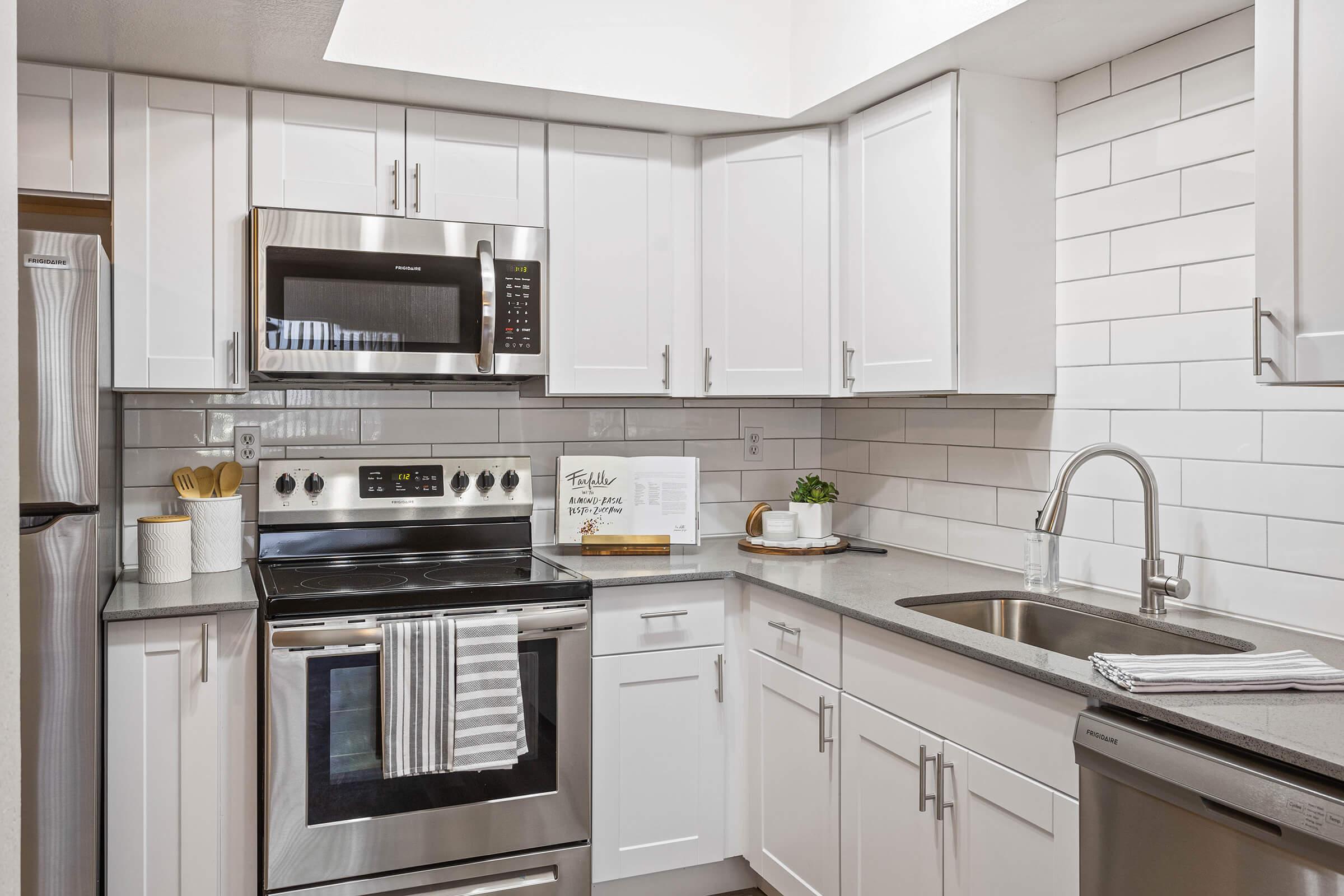 bright open kitchen with white cabinets, stainless steel appliances, and white tile backsplash