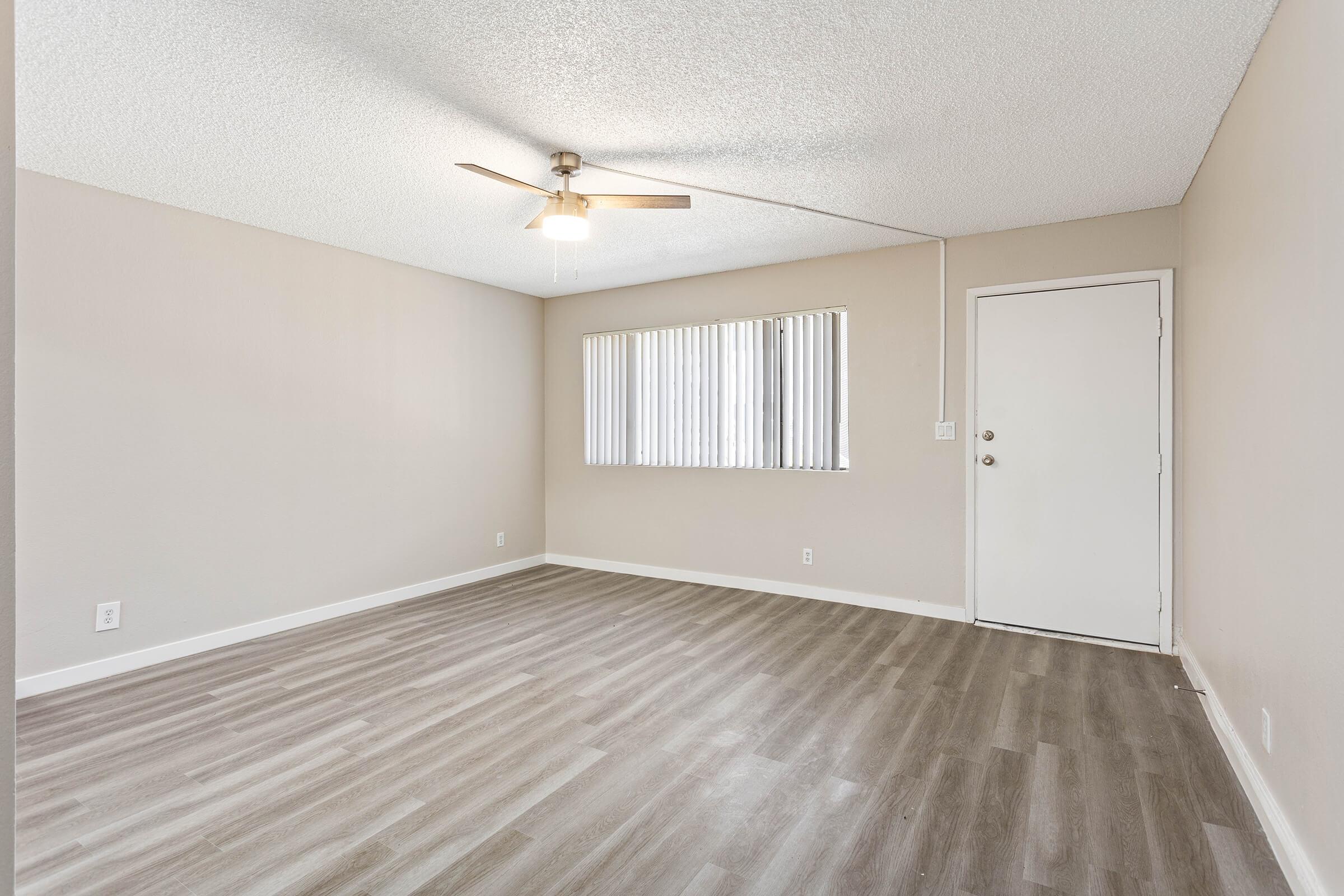 Open living room floor plan  with front door, ceiling fan, and front facing window