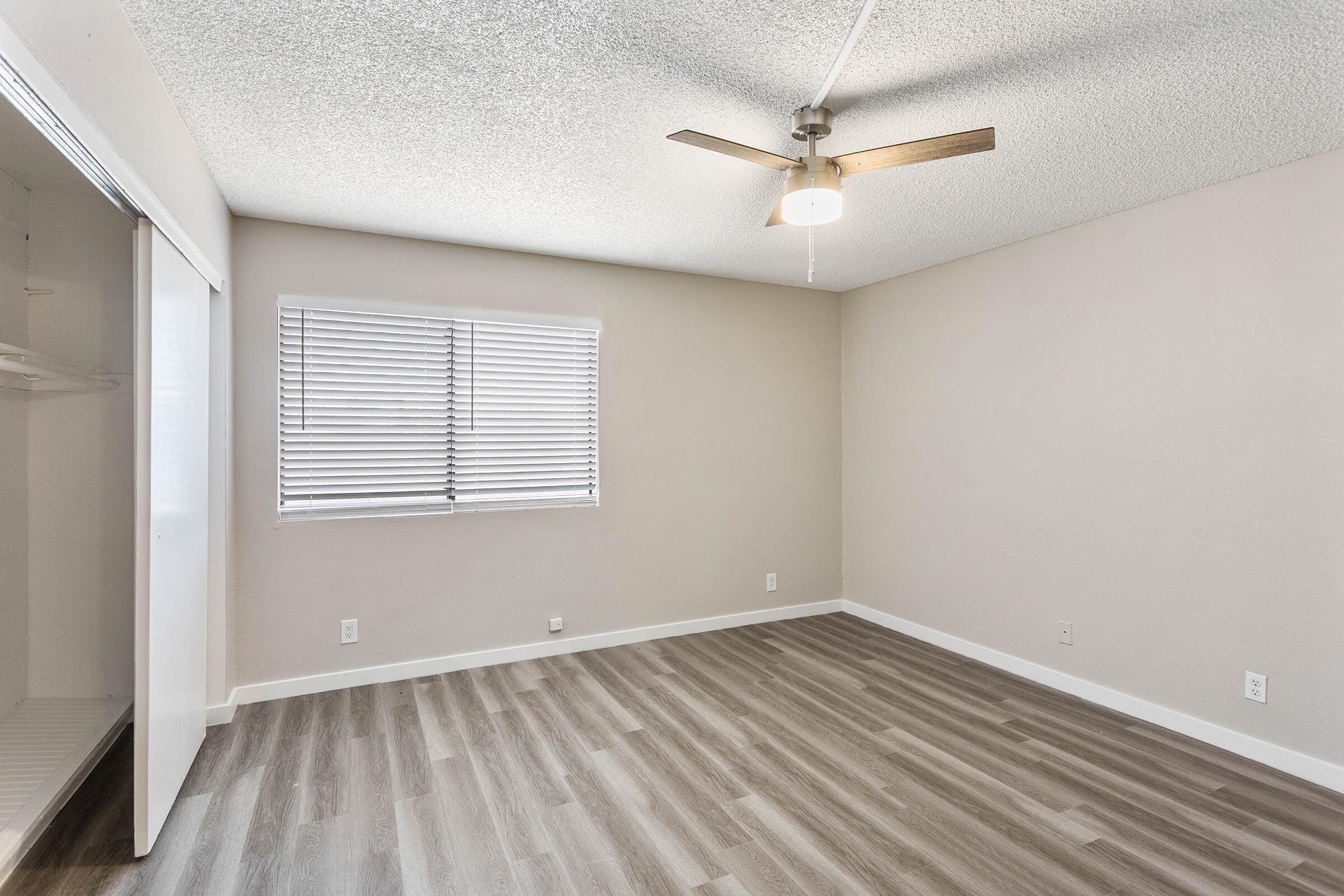 Open bright large main bedroom with wood flooring, window, and ceiling fan