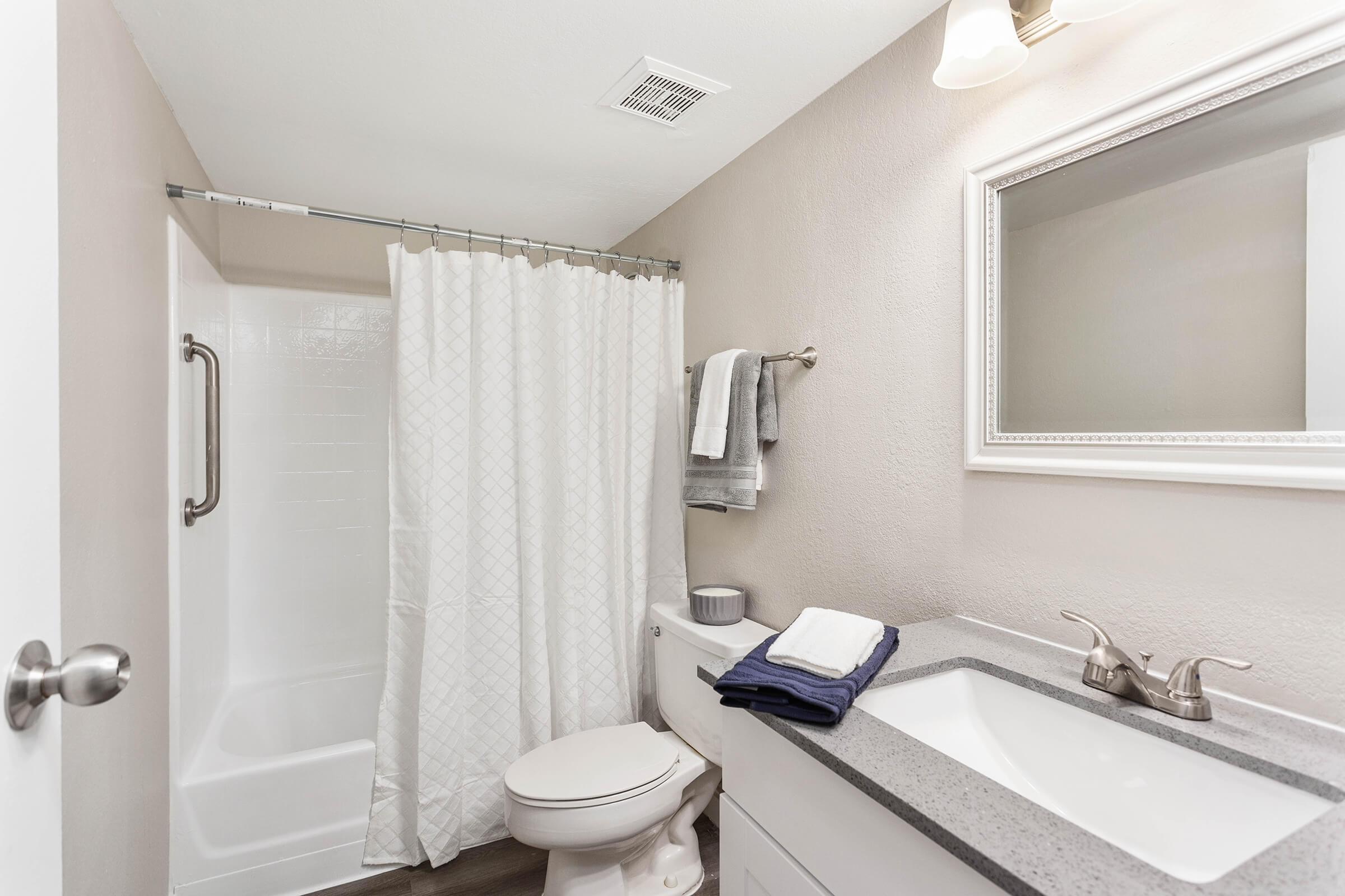 renovated bright bathroom with shower, toilet, quartz countertop sink, and small hand towels