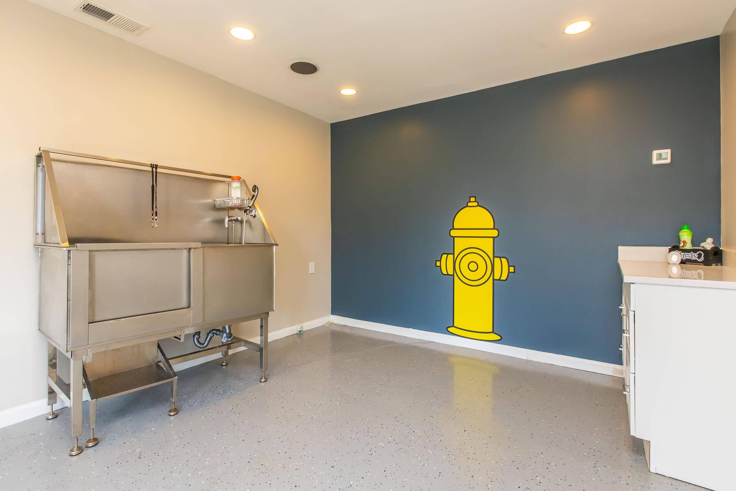 A clean interior space featuring a stainless steel sink and a yellow fire hydrant graphic on a dark blue accent wall. The floor has a polished, light-colored finish, and there are minimal decorations or furnishings, creating an open and bright environment.