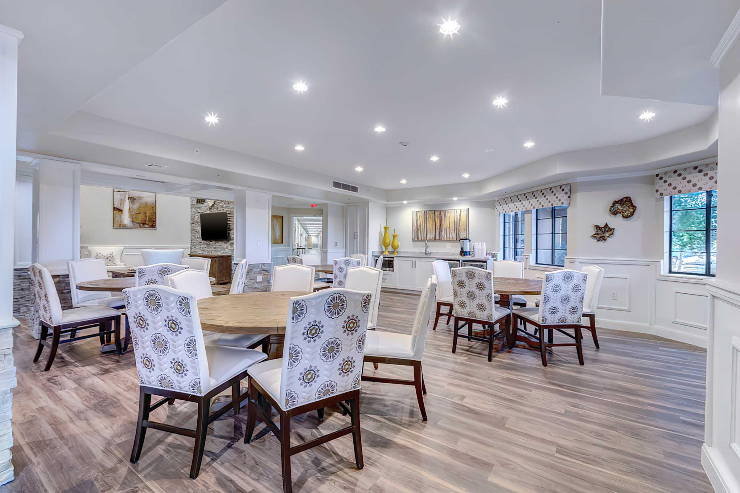 A spacious dining area with multiple round tables surrounded by upholstered chairs. 