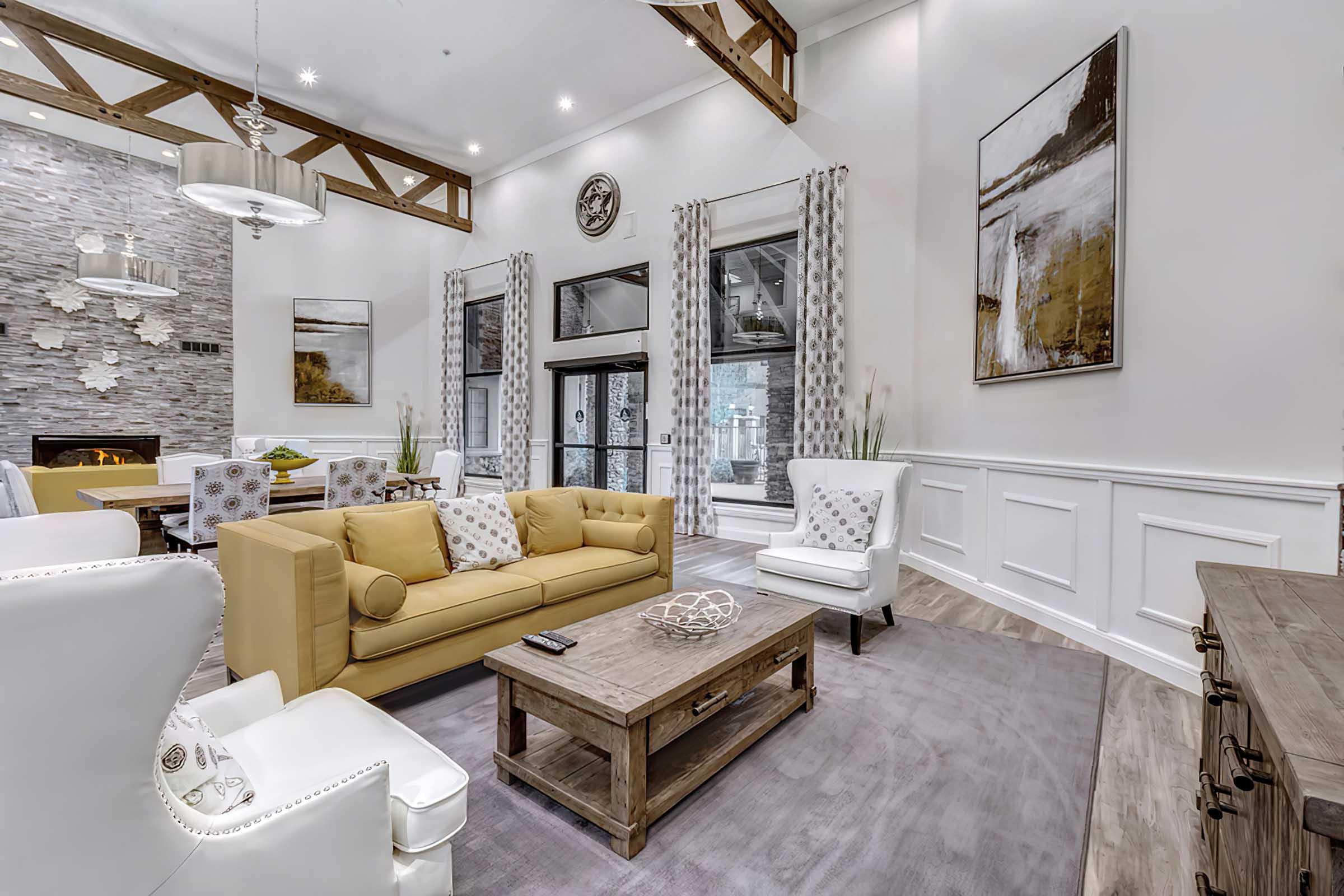 Spacious modern living room featuring a yellow sofa, white armchairs, and a wooden coffee table. 