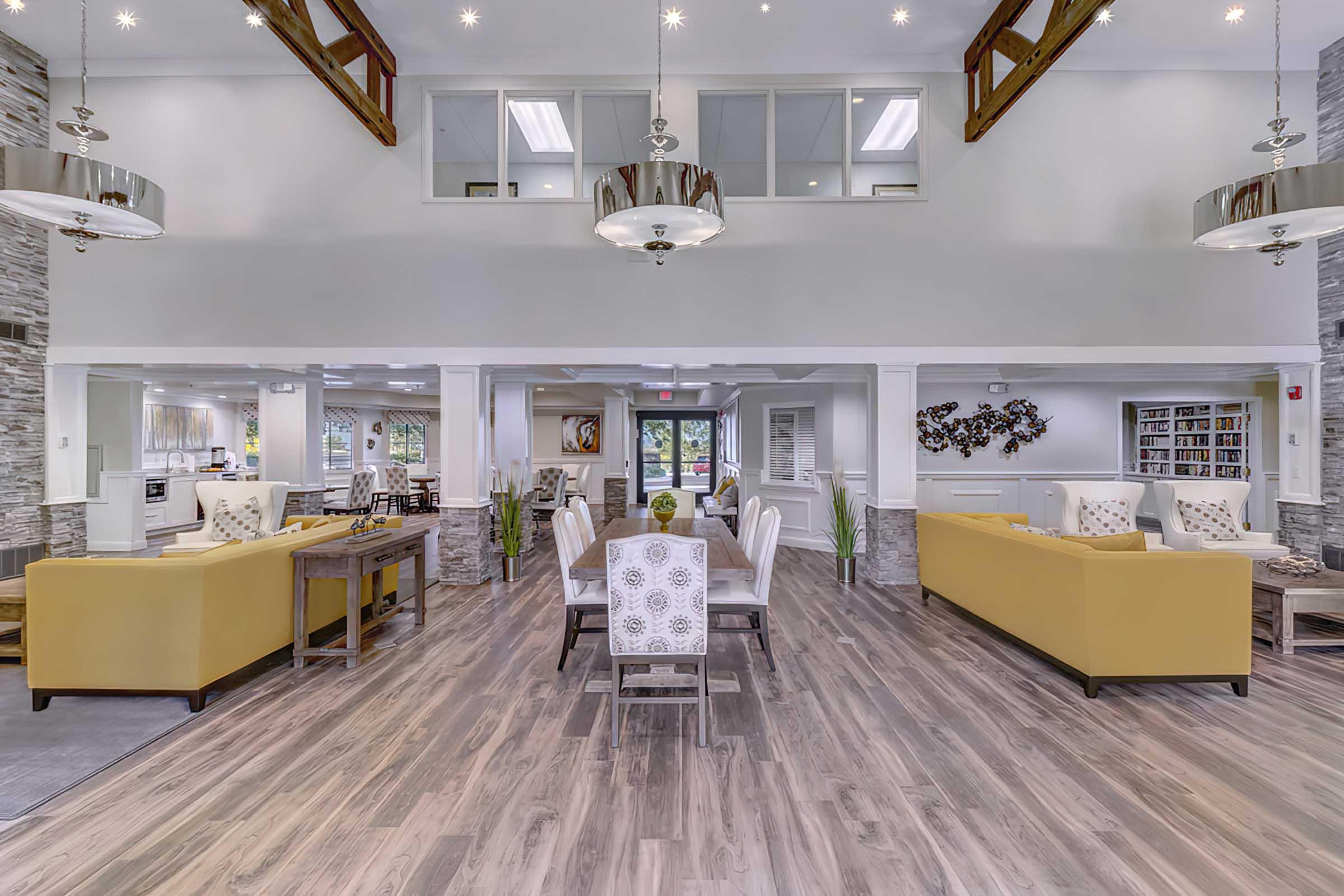 A spacious and modern communal area featuring large windows, high ceilings with wooden beams, and stylish lighting fixtures. 