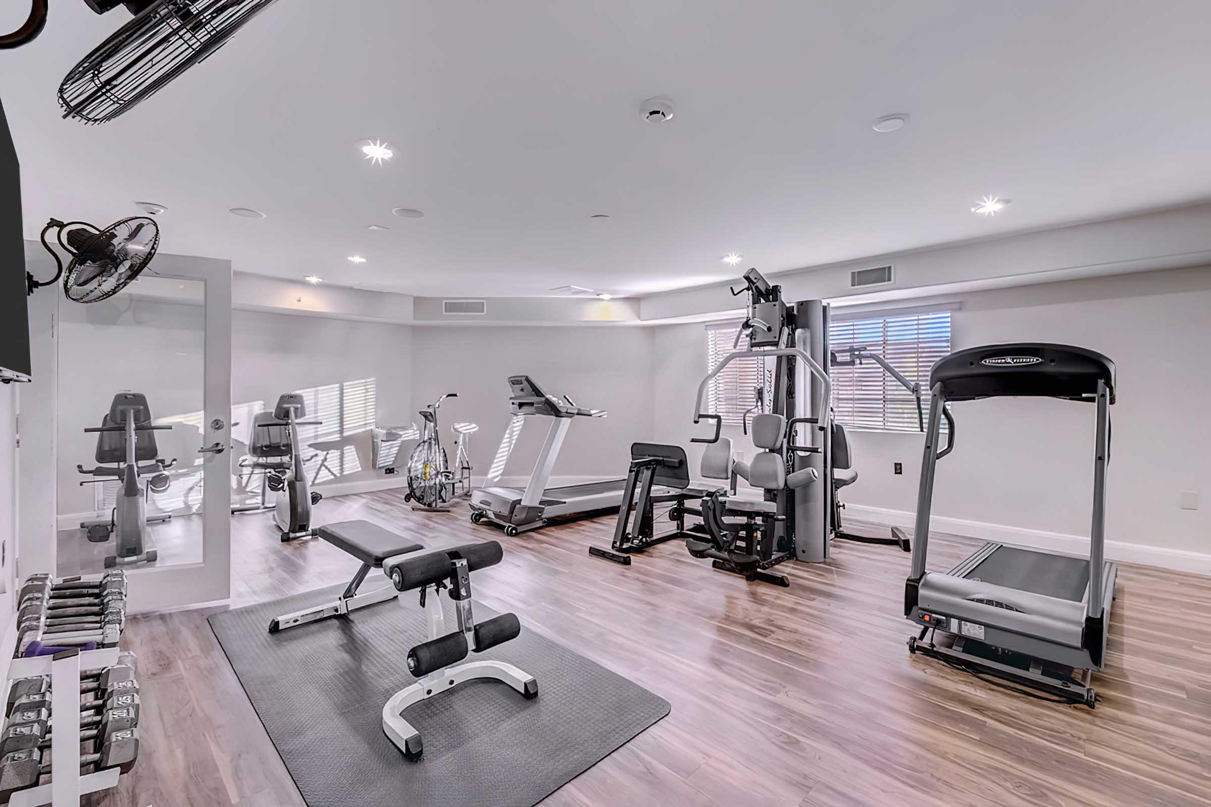 A modern home gym featuring various exercise equipment including a treadmill, stationary bike, weight bench, and multi-functional strength machines. 