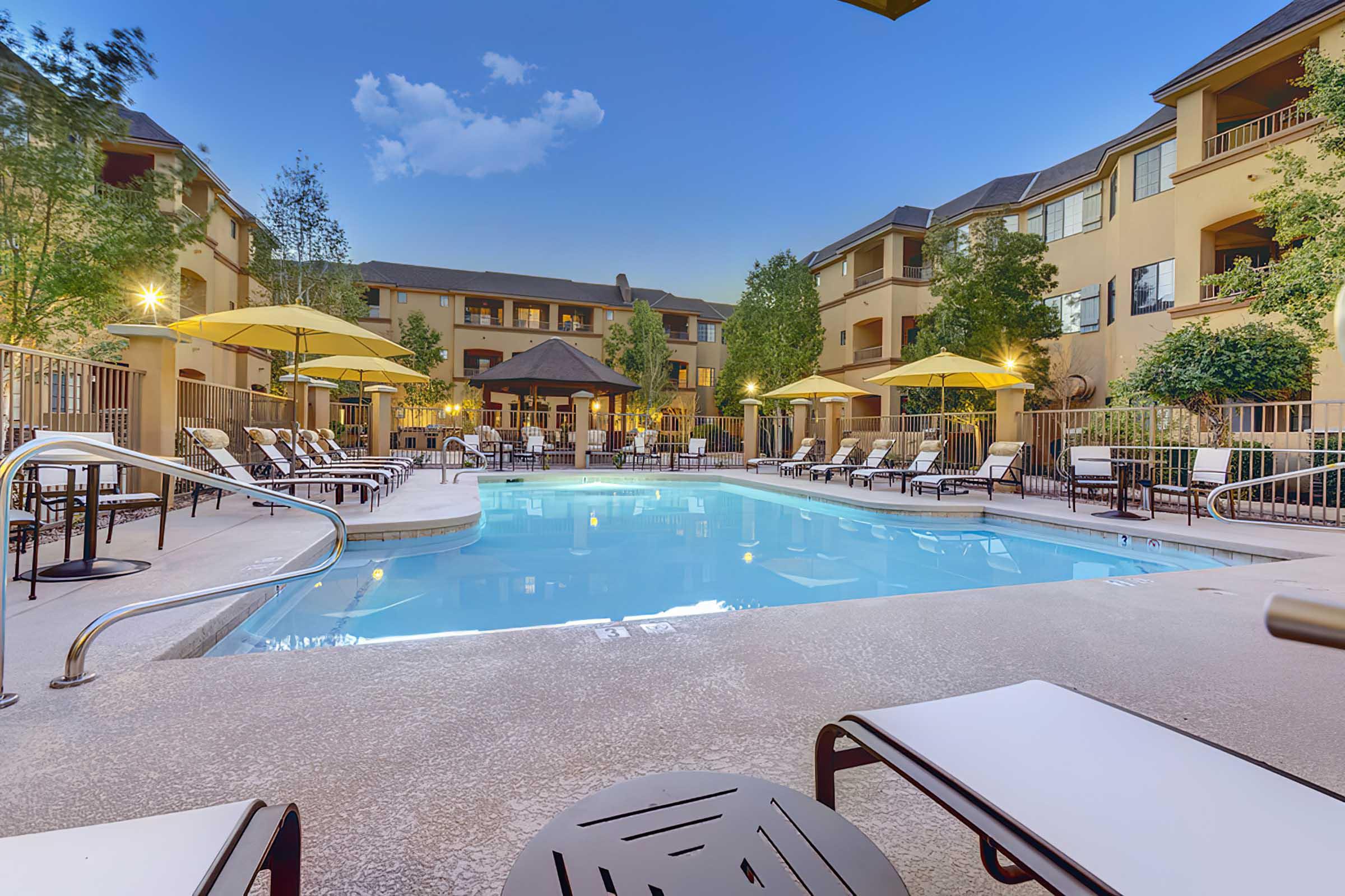 A serene pool area at dusk, featuring clear blue water, lounge chairs, and yellow umbrellas.