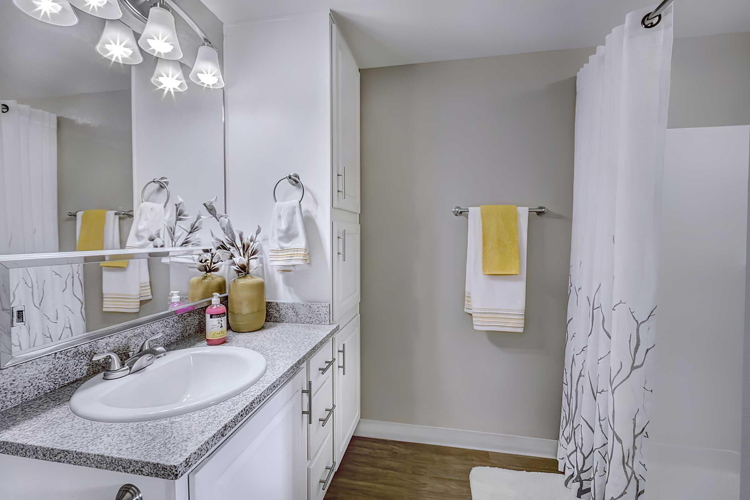 A modern bathroom featuring a granite countertop sink with a mirror above, white cabinets, and a neutral wall color. T