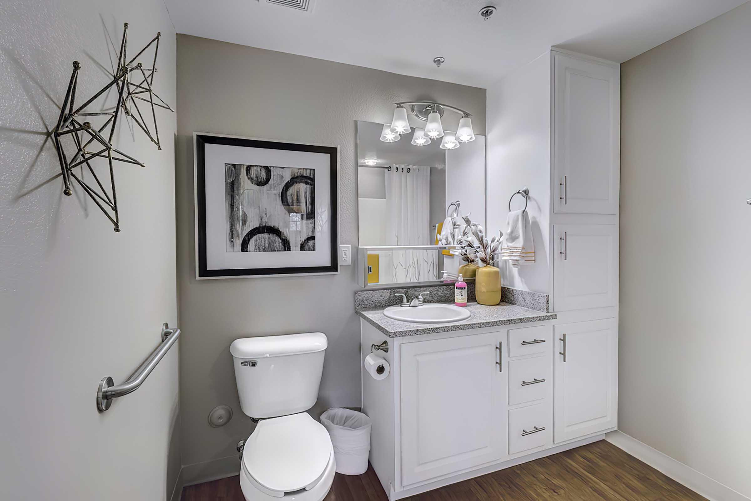  A modern bathroom featuring a white toilet, a sink with a gray countertop, a large mirror, and stylish wall decor. 