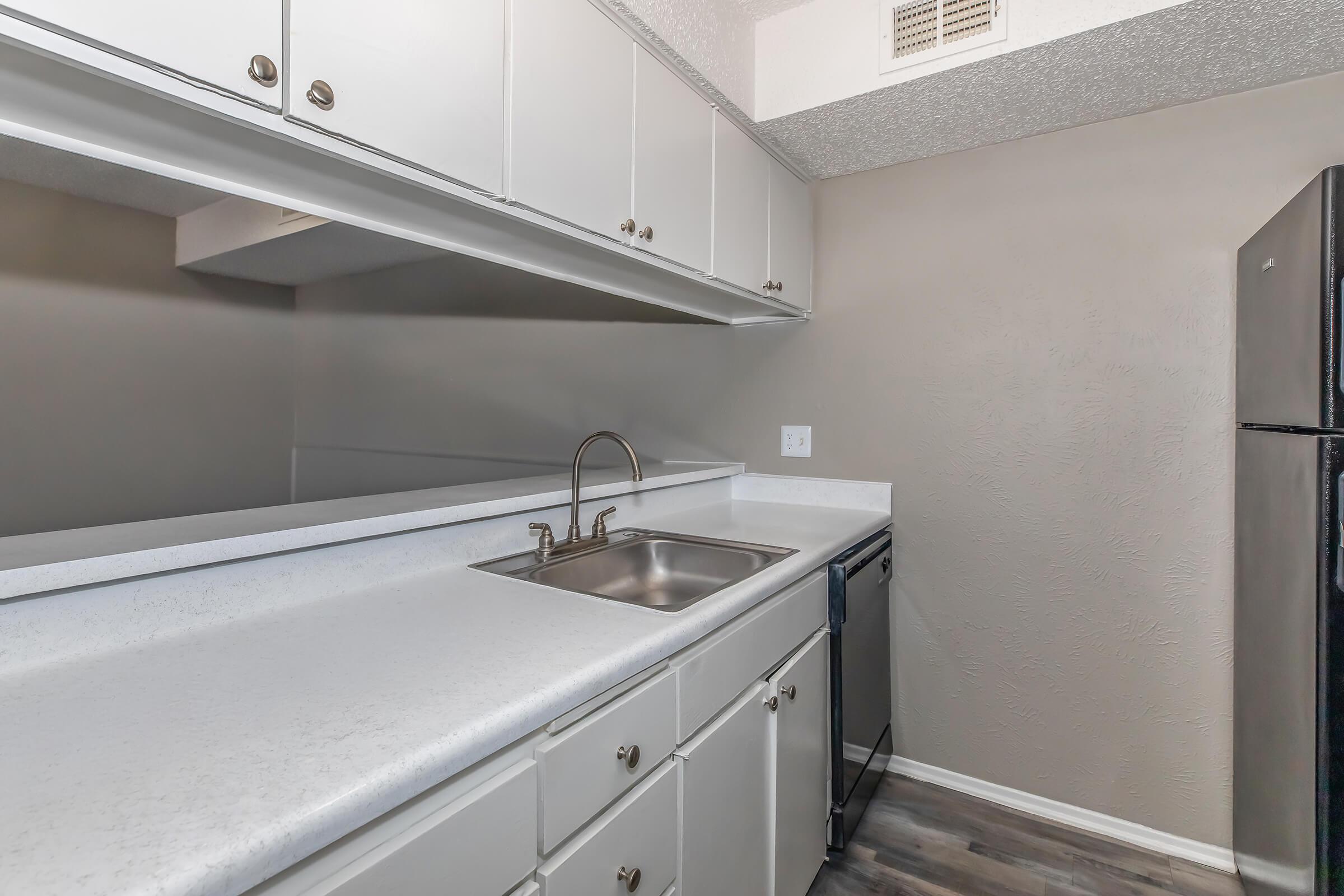 Modern kitchen featuring white cabinets, a stainless steel sink, a black refrigerator, and a dishwasher. The countertops are light-colored, and the walls have a neutral tone, creating a clean and inviting atmosphere.