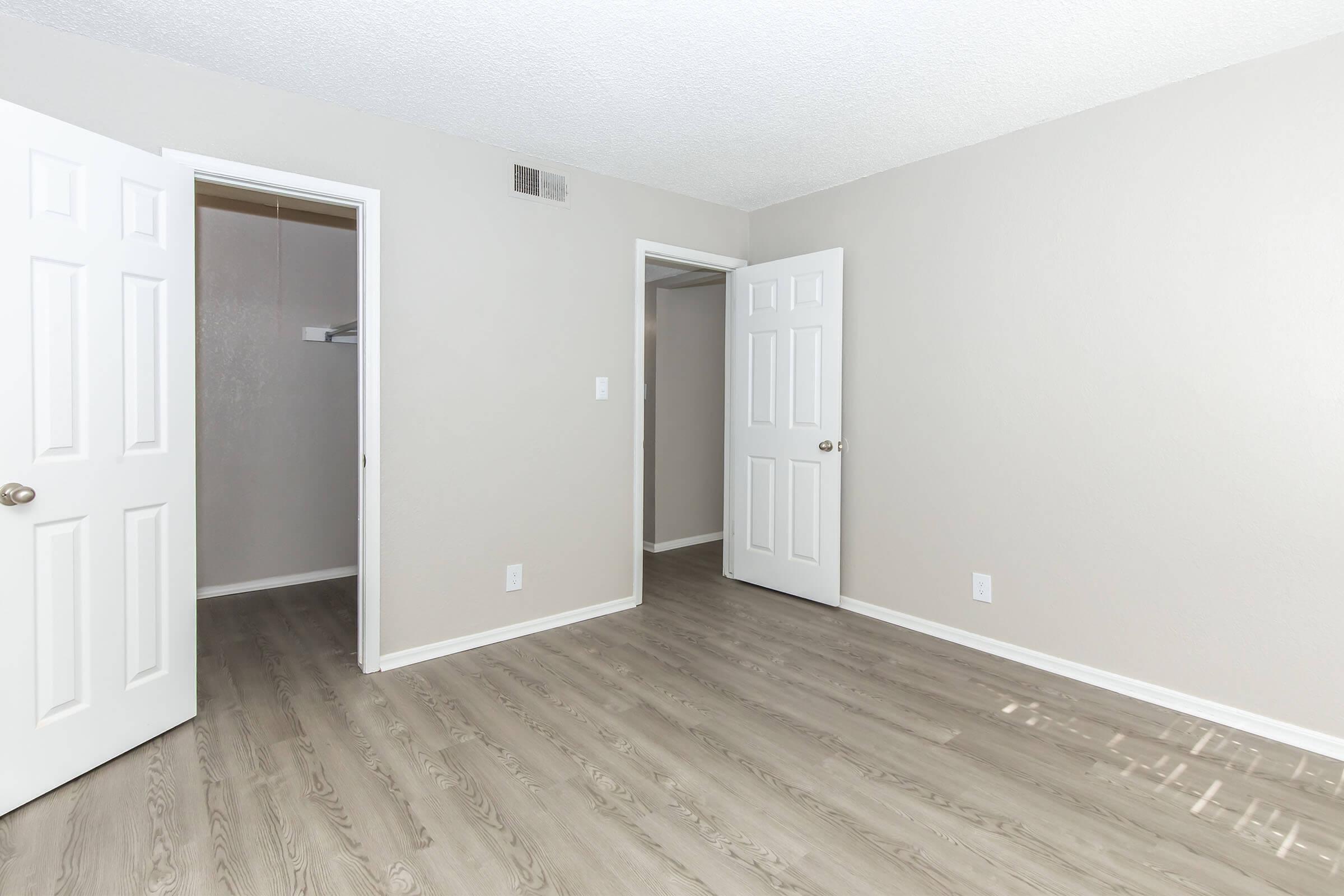 A vacant room featuring light gray walls and a textured ceiling. There are two open white doors, one leading to a closet. The floor is a light wood laminate, and natural light comes in, creating a bright ambiance. The space is clean and ready for furnishing.