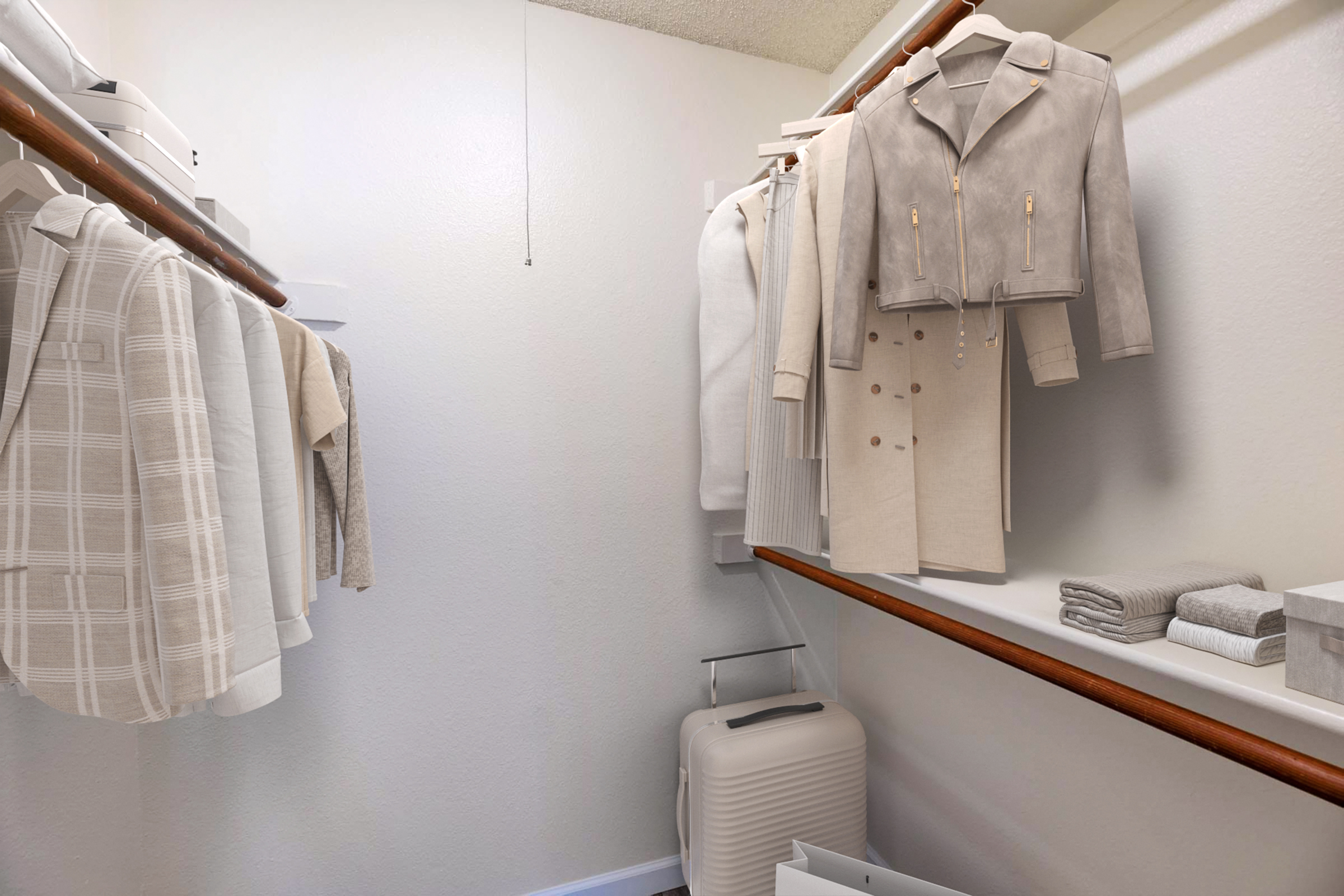 A well-organized closet featuring light-colored clothing on wooden hangers, including a stylish jacket and various garments. There are neatly folded towels and a sleek suitcase on the floor, emphasizing a minimalist and tidy aesthetic. The walls are plain white, enhancing the clean look of the space.