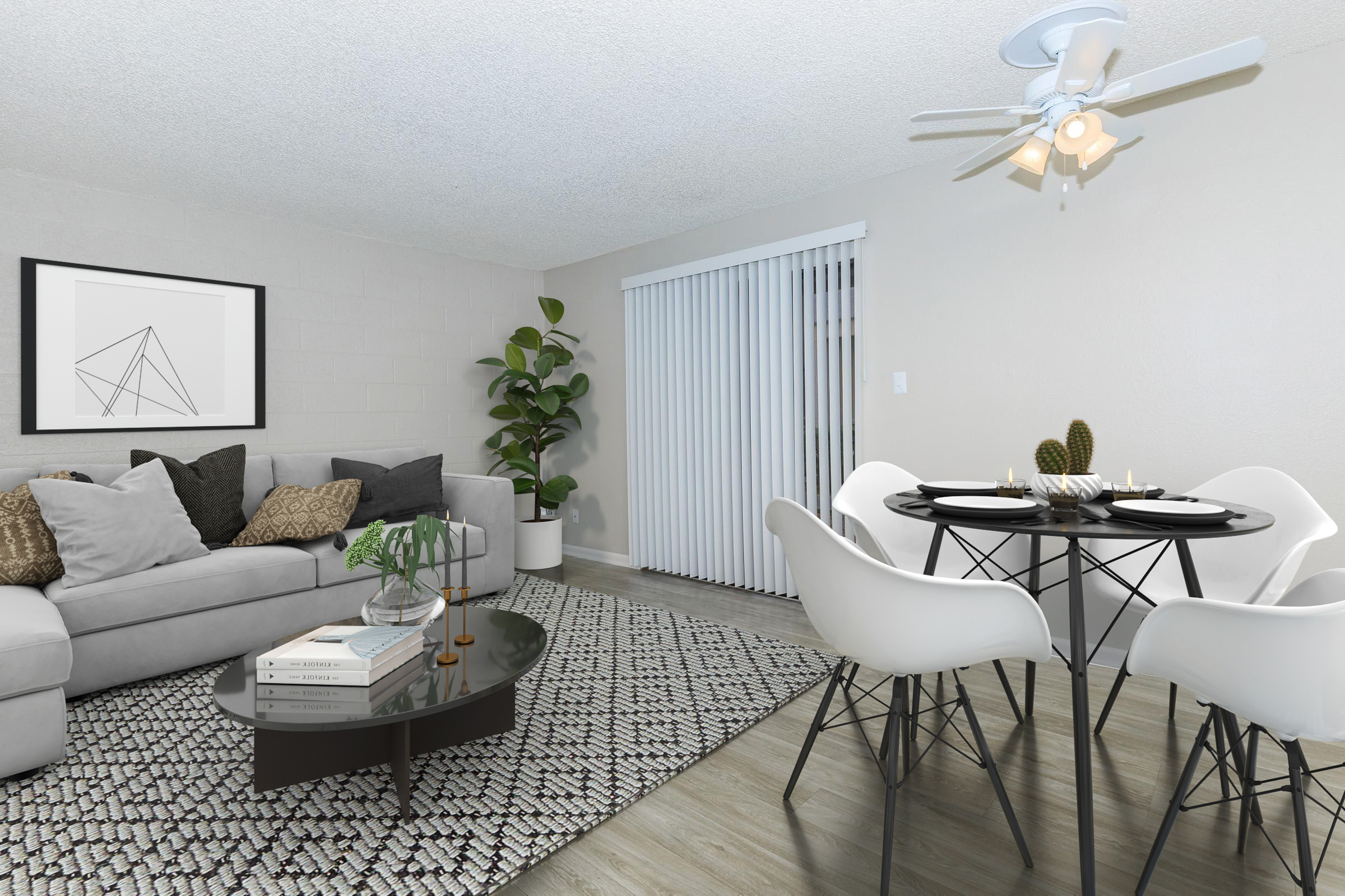 A modern living space featuring a light gray sectional sofa with decorative pillows, a glass coffee table, and a stylish rug. In the background, a dining area with a round table and white chairs, complemented by a potted plant and sliding glass doors that lead outside. A minimalist wall art adds a touch of sophistication.