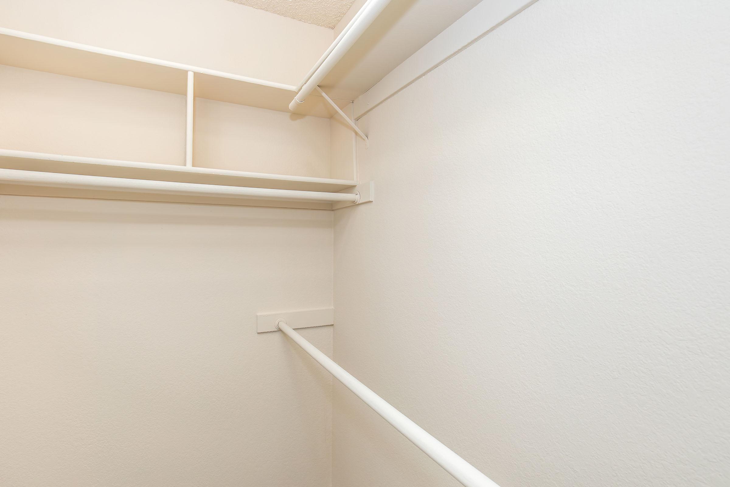 A clean, empty closet with white walls and a white hanging rod. The shelving above the rod is also white, creating a minimalist and simple design.