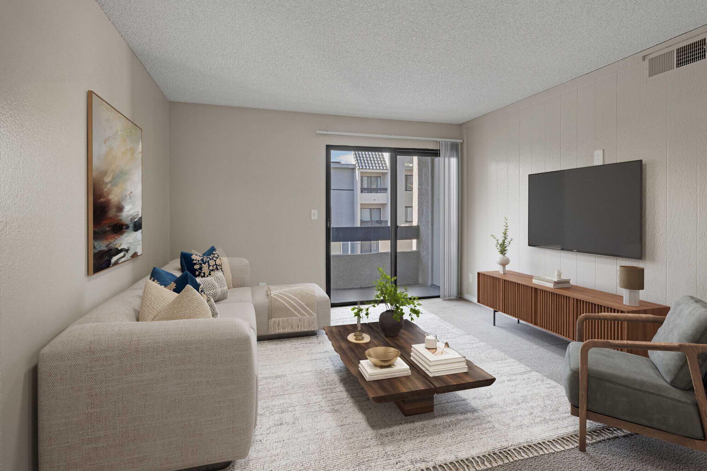 A modern living room featuring a light-colored sectional sofa with decorative pillows, a wooden coffee table with books and a plant, and a mid-century style armchair. The room has a large window with balcony access, soft lighting, and minimalistic decor, creating a cozy and inviting atmosphere.