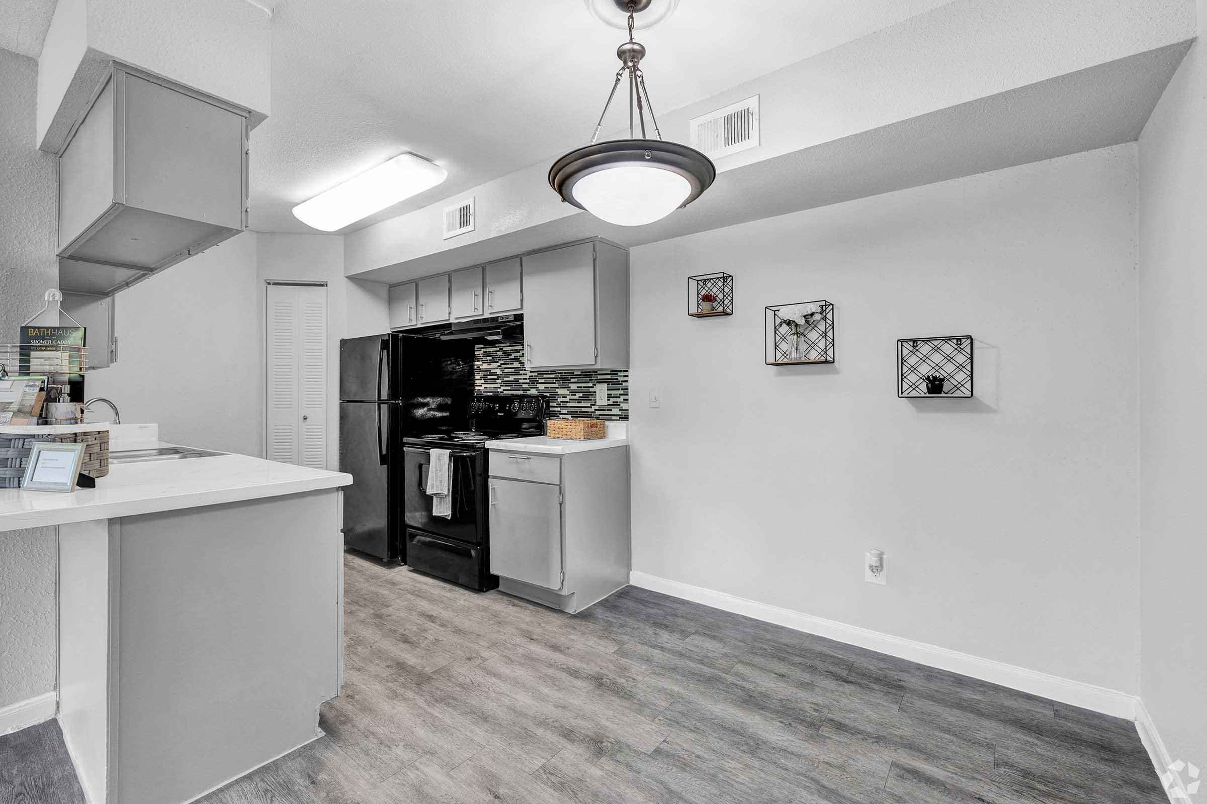 Modern kitchen with gray cabinetry, a black refrigerator, and a white countertop. Features pendant lighting and decorative wall art. The flooring is light wood, adding to the contemporary aesthetic.