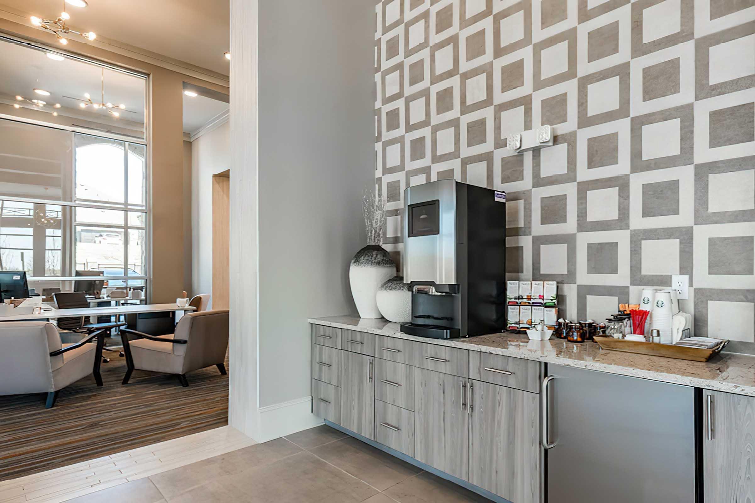 A modern interior space featuring a coffee station with a sleek black coffee maker, decorative vases, and various condiments.