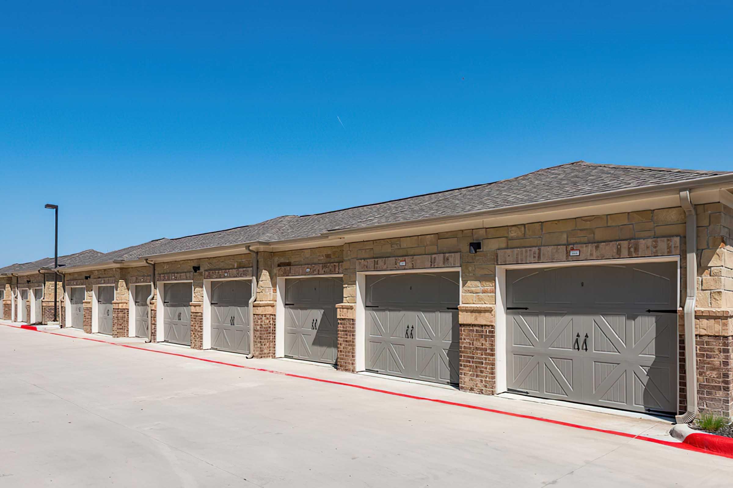 A row of beige garages with horizontal doors, situated in a well-maintained area.
