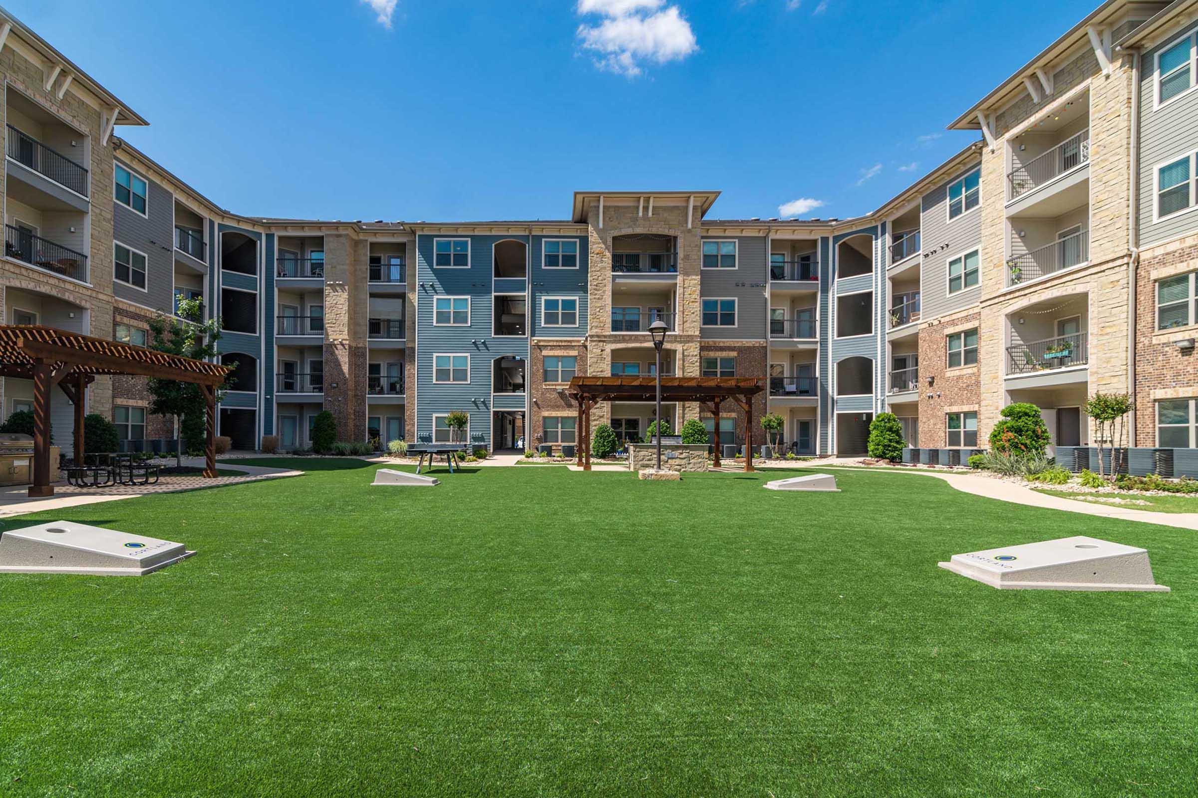 A spacious courtyard of an apartment complex featuring green artificial turf, a woode