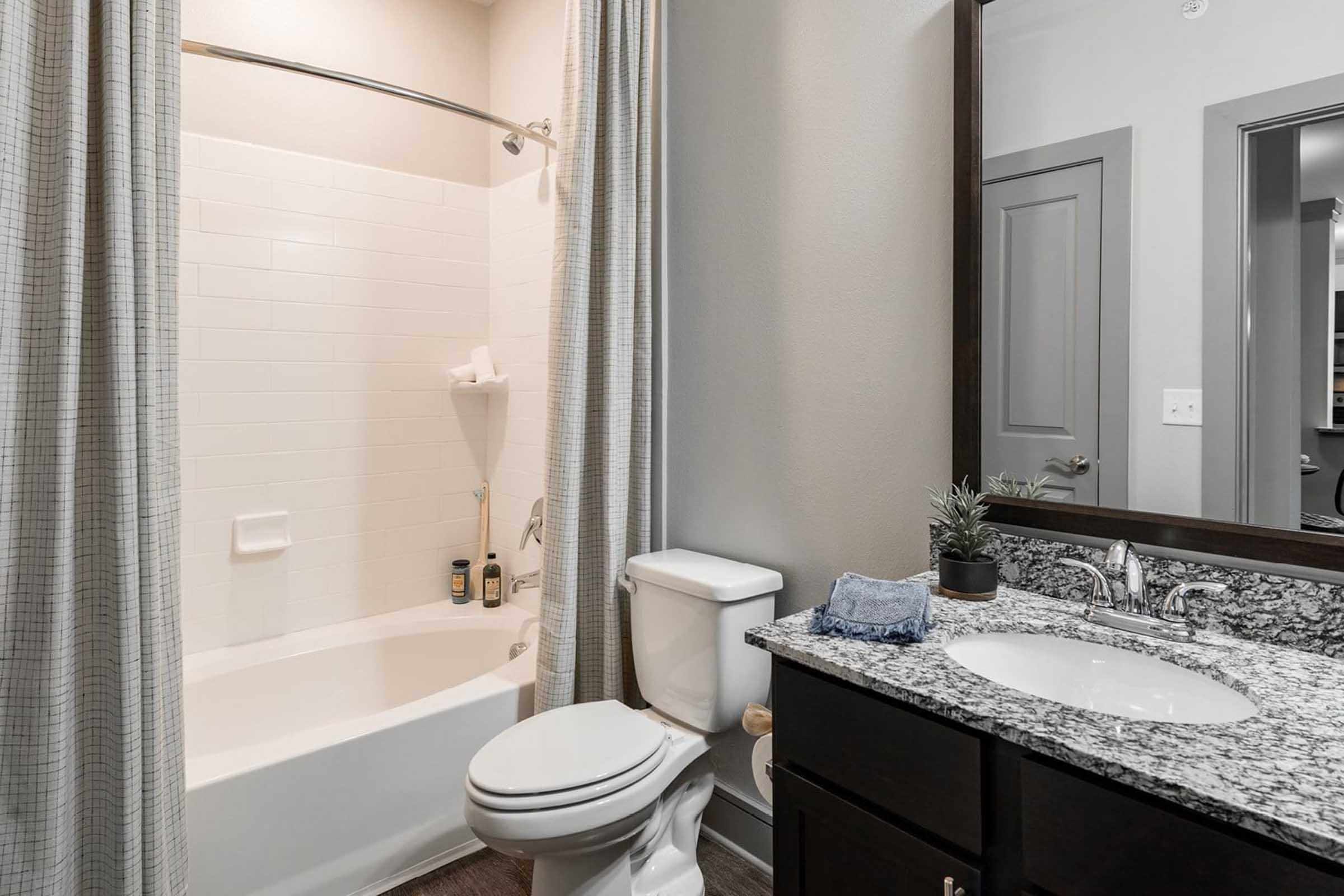 A modern bathroom featuring a bathtub with a shower curtain, a toilet, and a sleek vanity with a granite countertop.