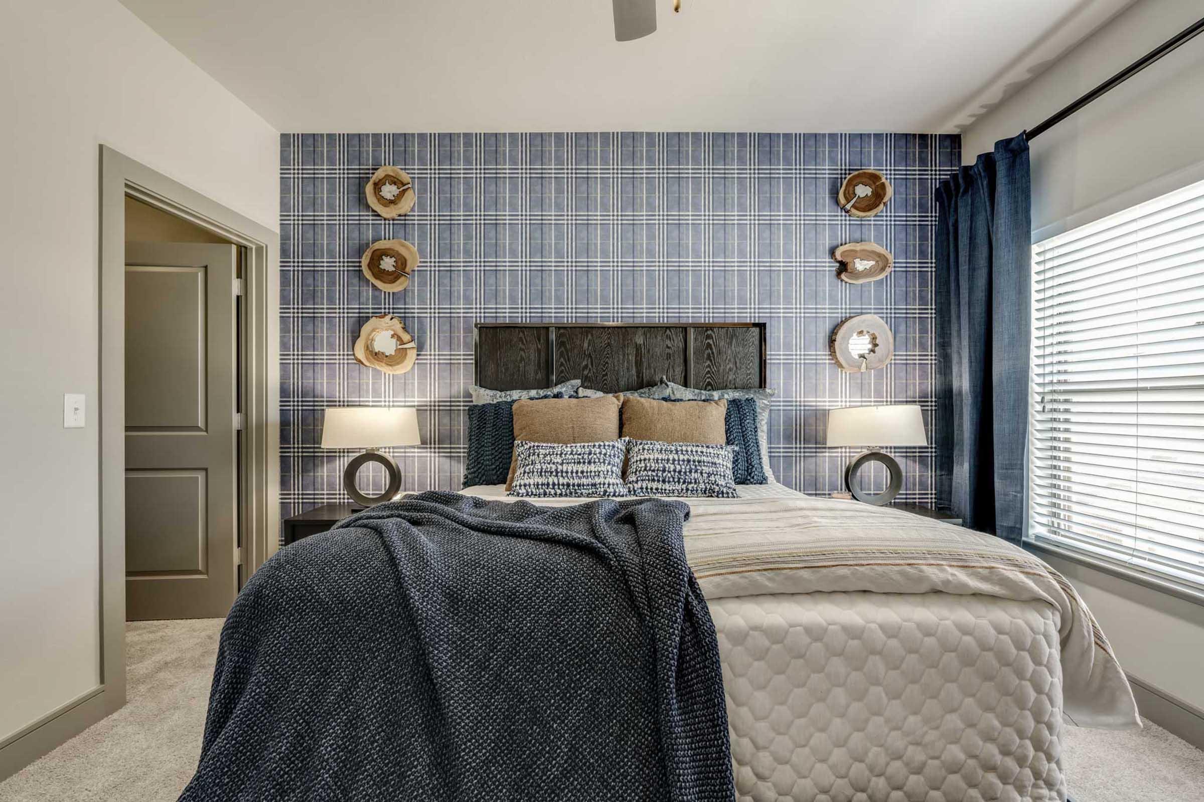 A cozy bedroom featuring a plaid accent wall, a queen-sized bed with decorative pillows, and a textured blanket.