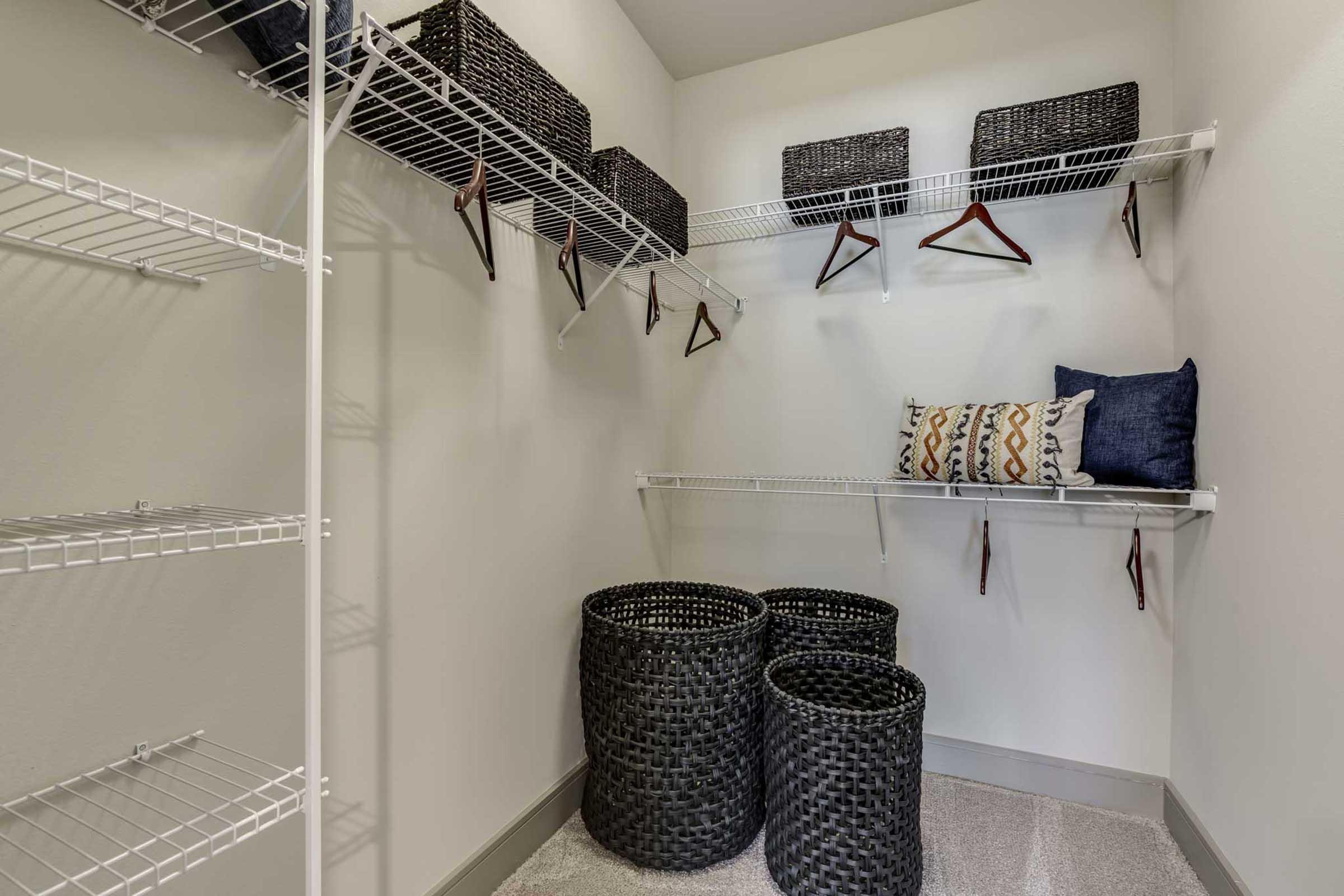 Empty closet with white wire shelving, dark woven storage baskets on the shelves, and two round black baskets on the floor.