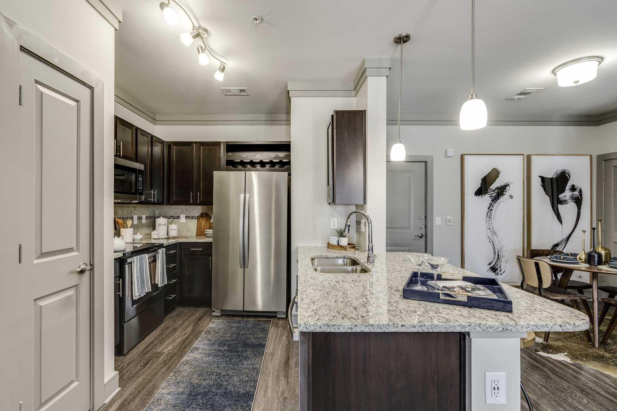 Modern kitchen featuring dark wood cabinets, stainless steel appliances, and a large granite island.